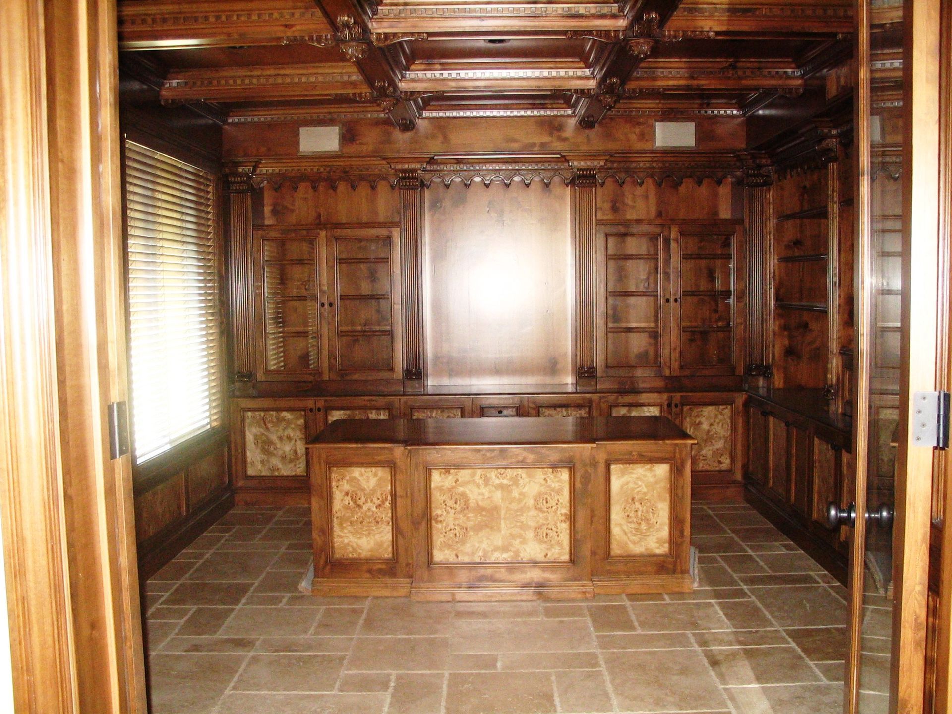 Luxurious wood-paneled office with built-in shelves, desk, and a stone tile floor.