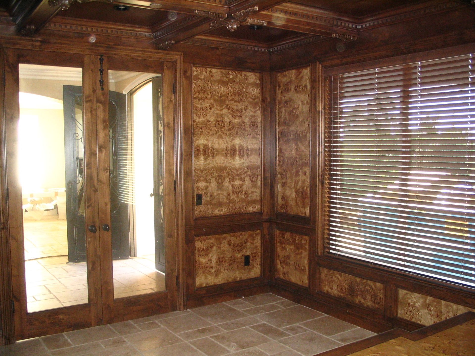 Dark paneled room with mirrored doors, patterned walls, a window with blinds, and stone floor.