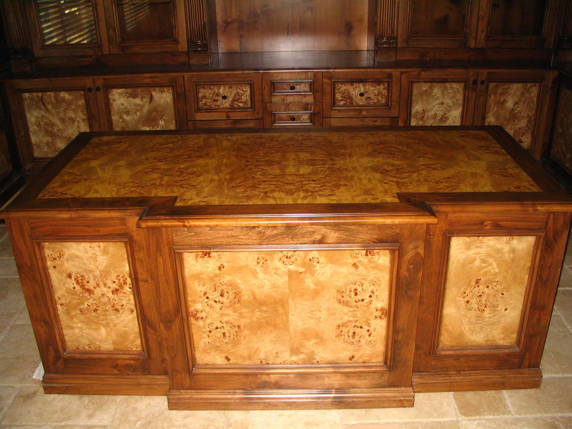 Wooden executive desk with burl wood panels and built-in hutch in a home office setting.