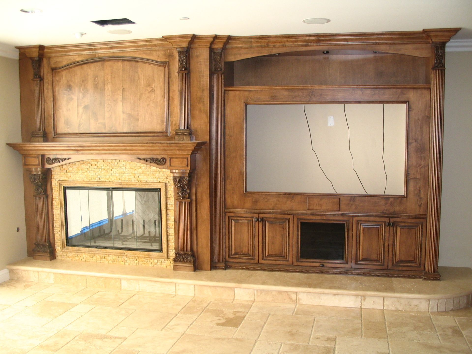 Built-in wooden entertainment center with fireplace and TV space, beige stone accents, and tiled floor.