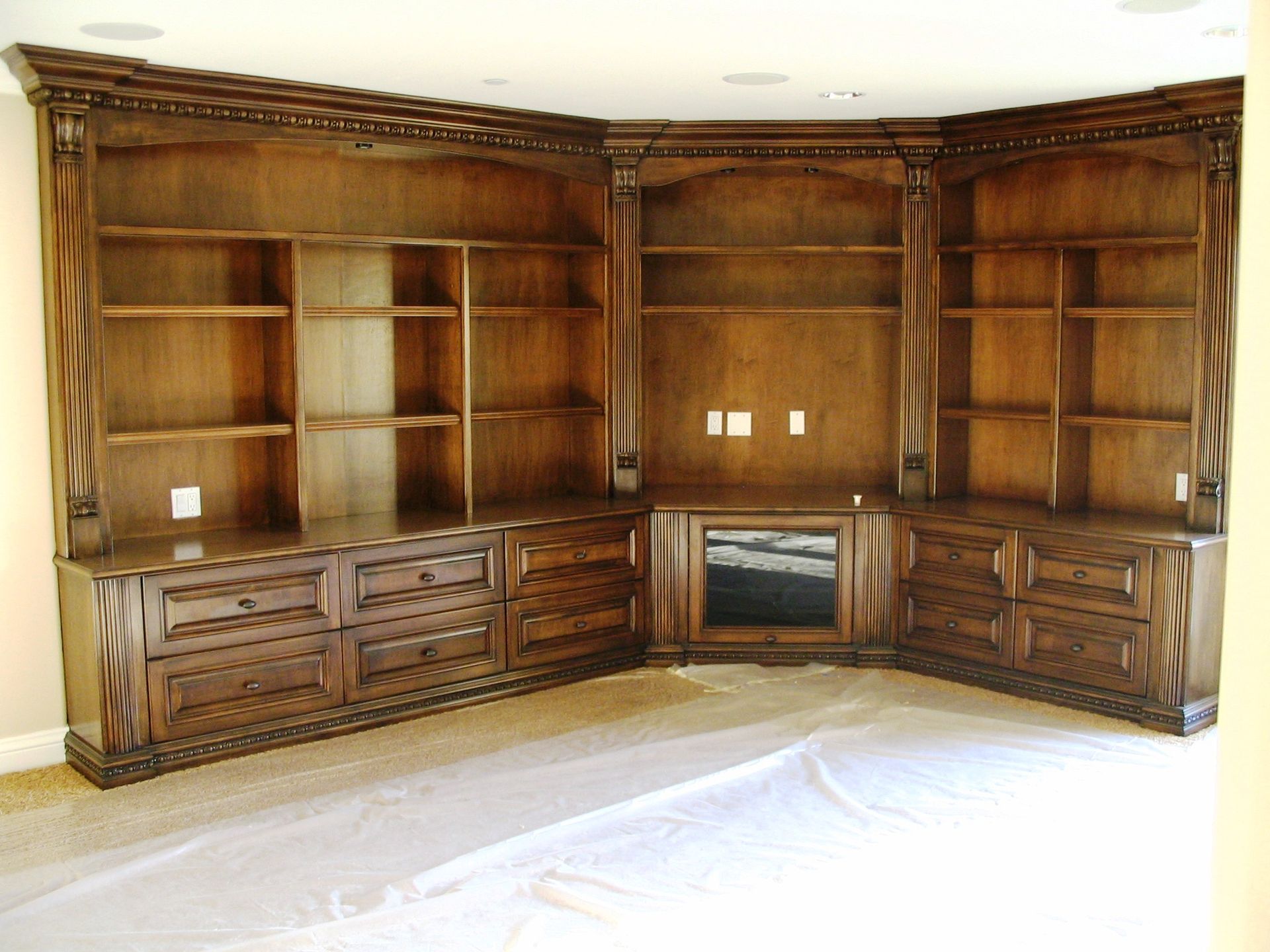 Built-in wooden corner shelving unit, brown, with drawers and display space.