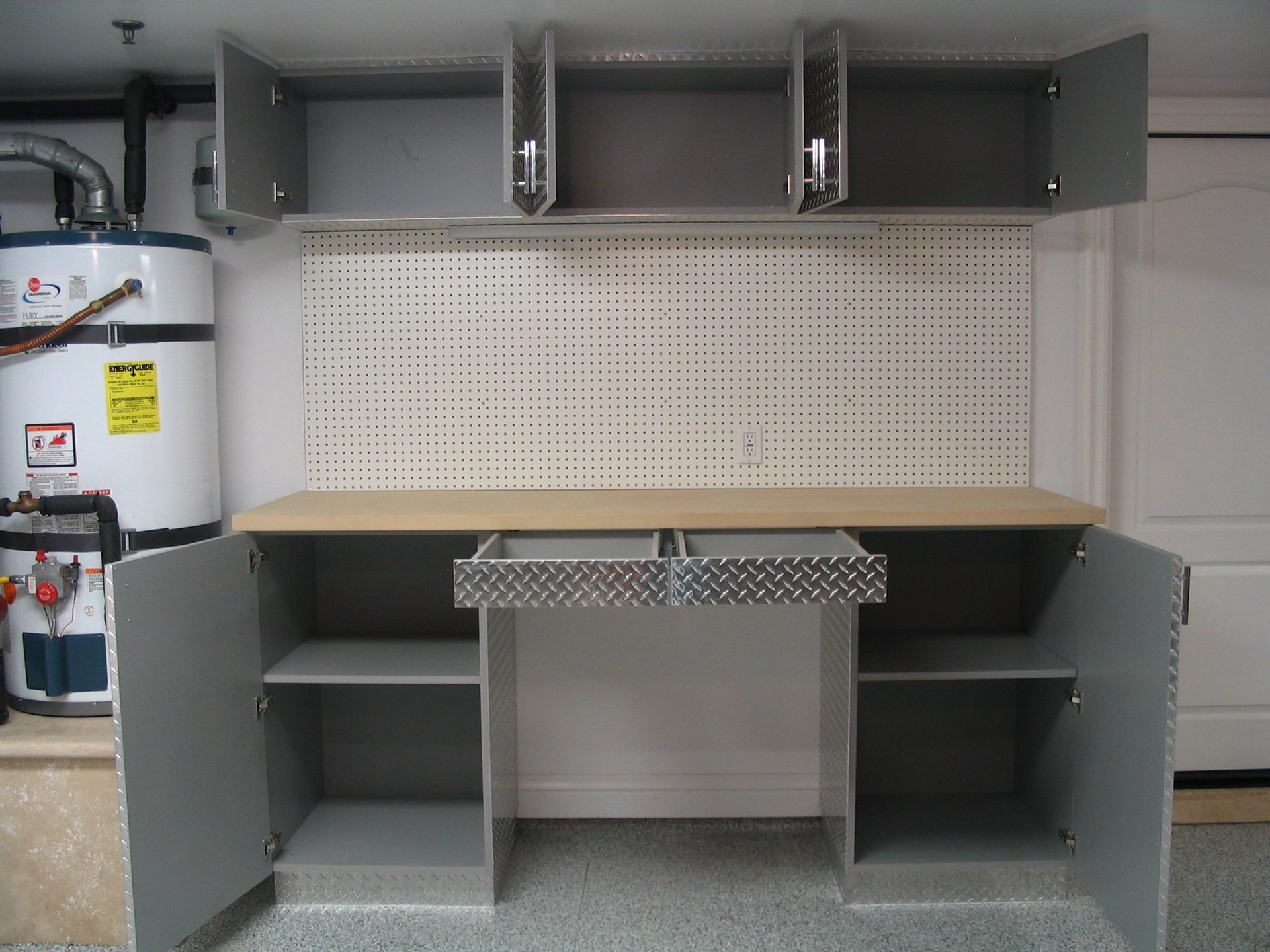 Garage workspace with gray cabinets and workbench, pegboard, water heater in the background.