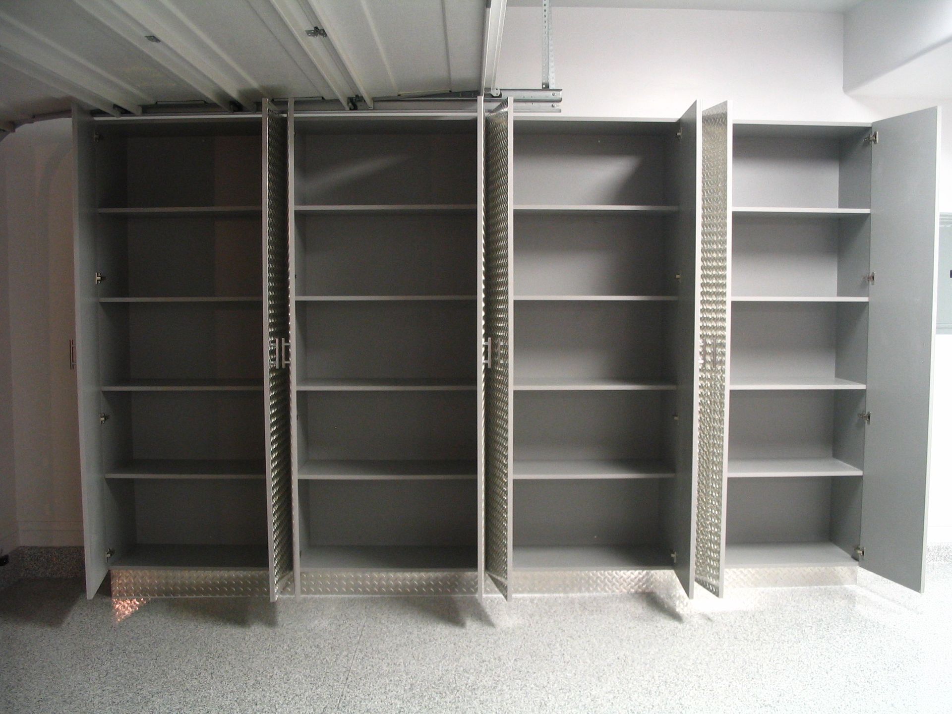 Four open, empty gray metal storage cabinets in a garage setting.