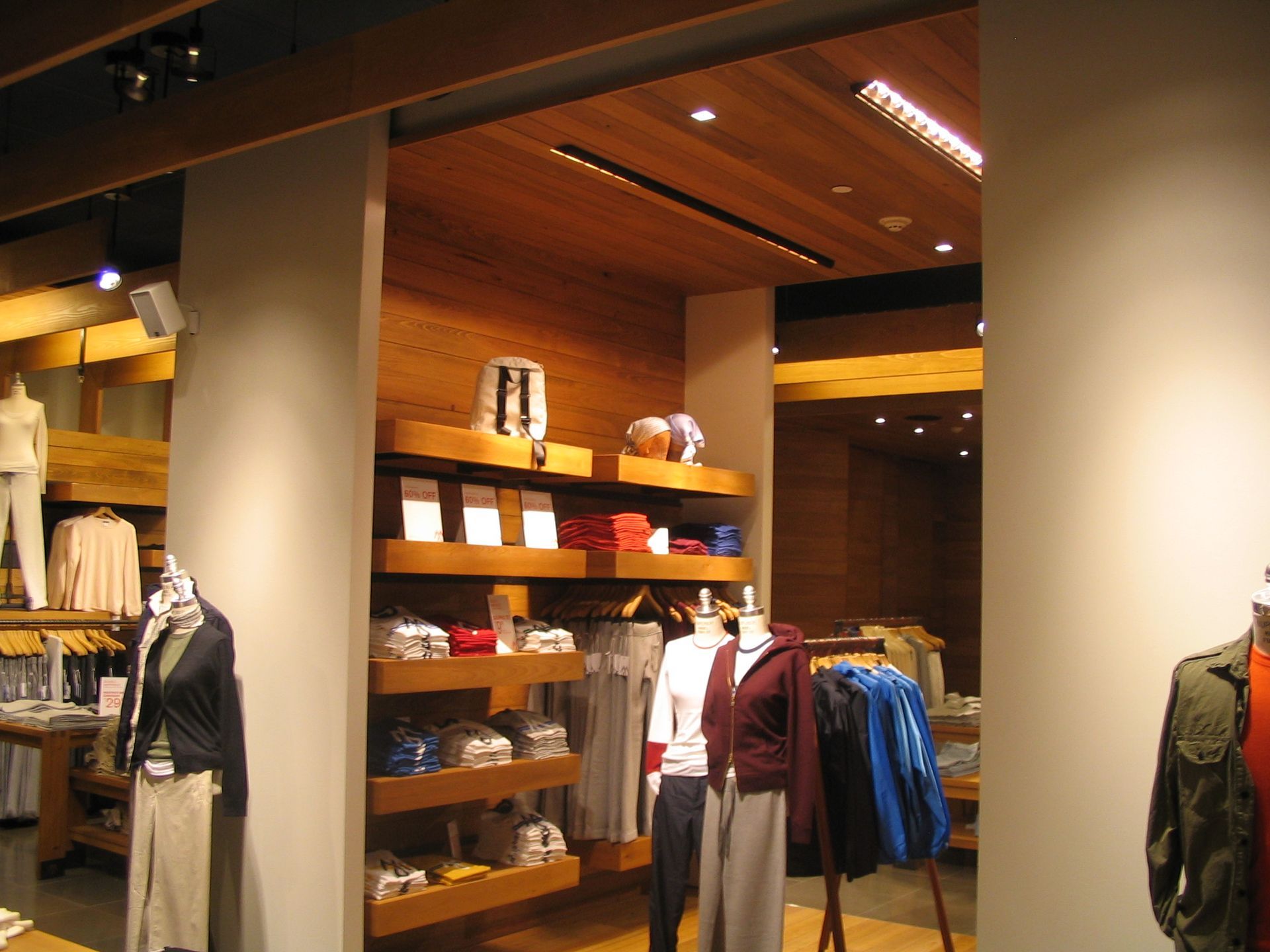 Clothing store interior with wooden shelves, displaying apparel. Mannequins wear shirts and pants.