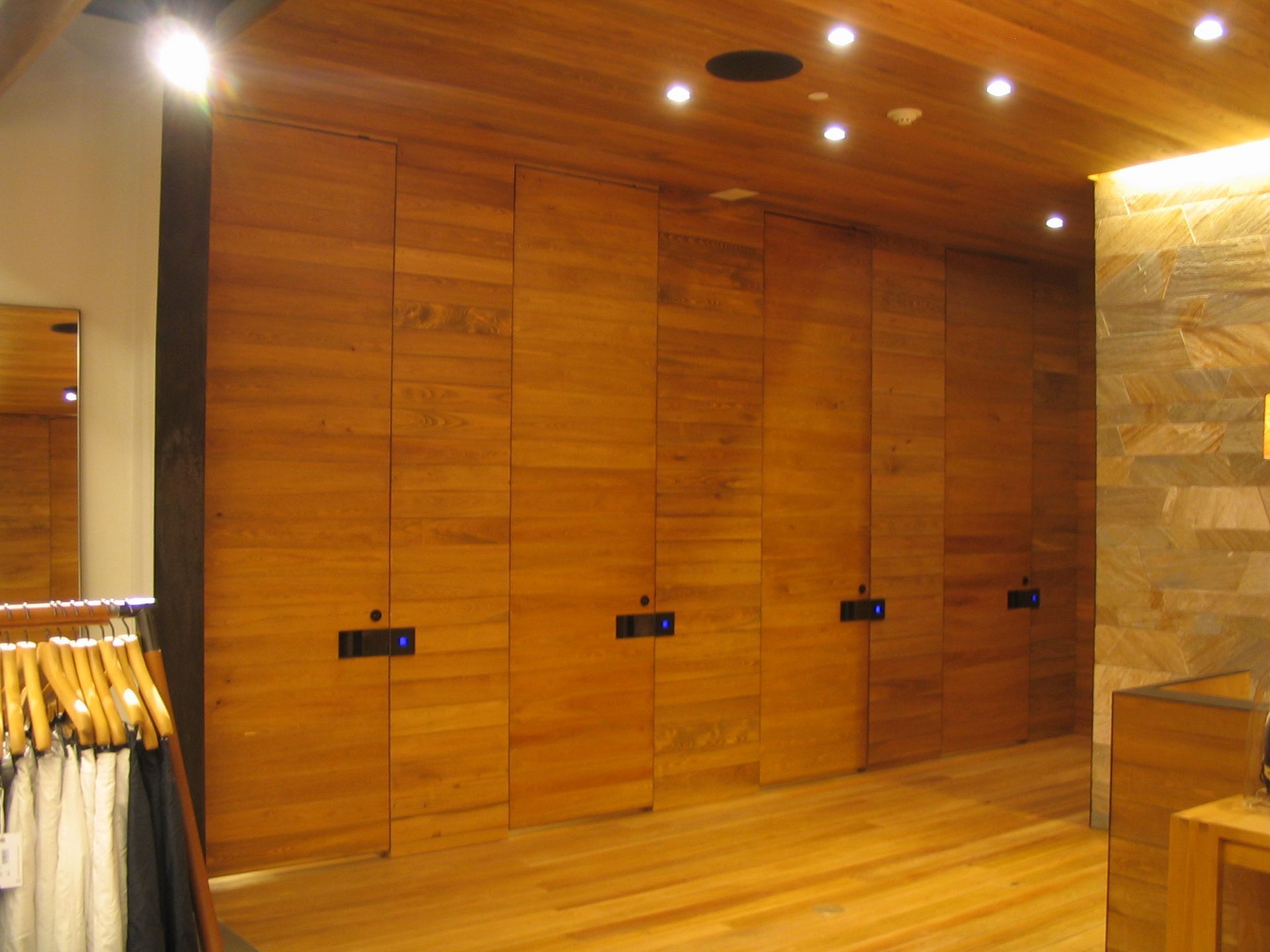 Wooden doors in a row, part of a wall; inside a store with wooden floor and ceiling, some lights.