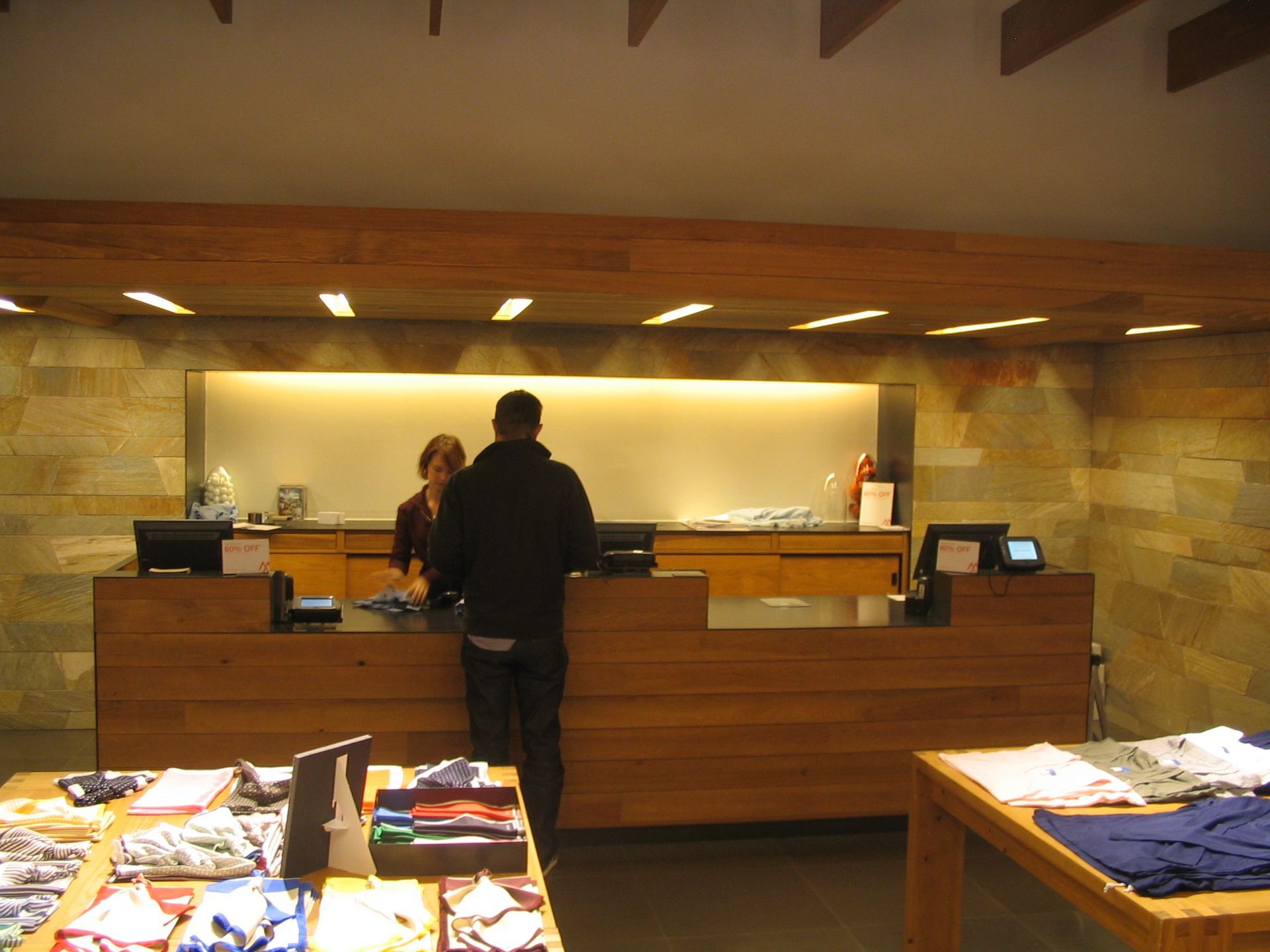 Man at checkout counter in a clothing store, interacting with the cashier. Store has wooden and stone decor.