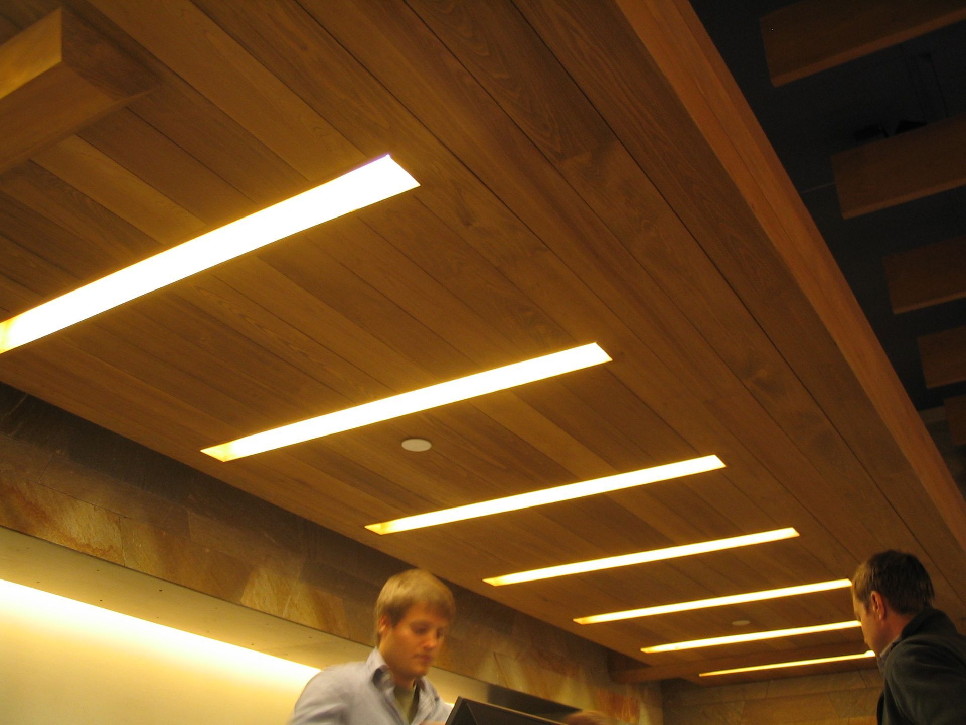 Wooden ceiling with recessed linear lights; two men stand below.