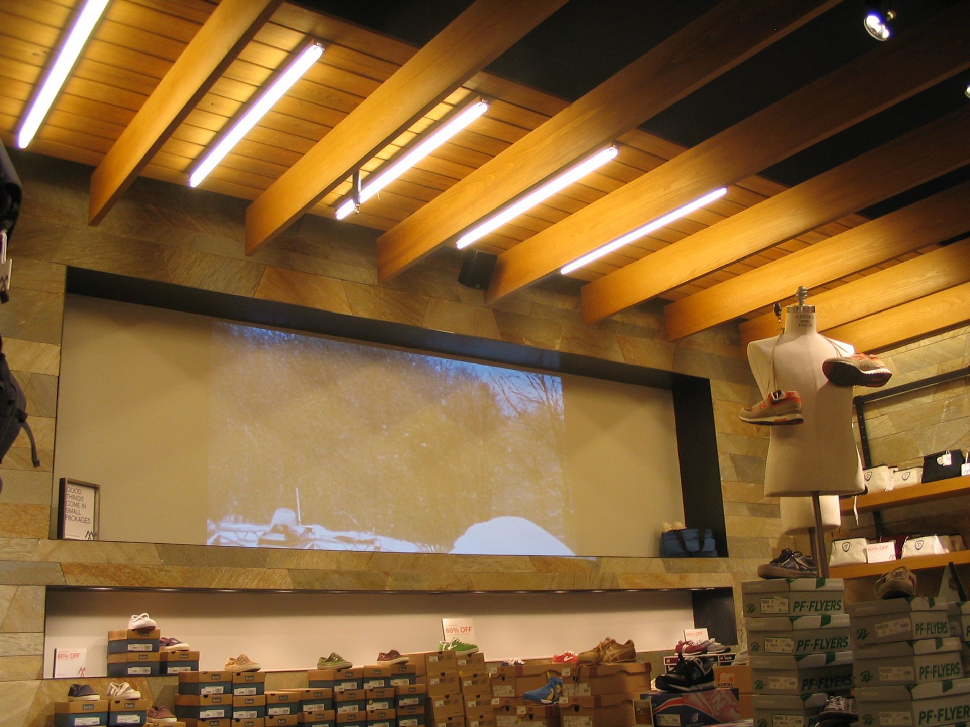 Shoe store interior with wooden ceiling beams, a video screen, and mannequin displaying shoes.