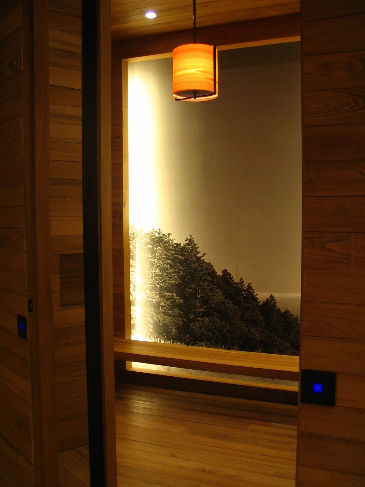 Wooden-paneled doorway framing a lit alcove with a landscape scene, bench, and orange lampshade.