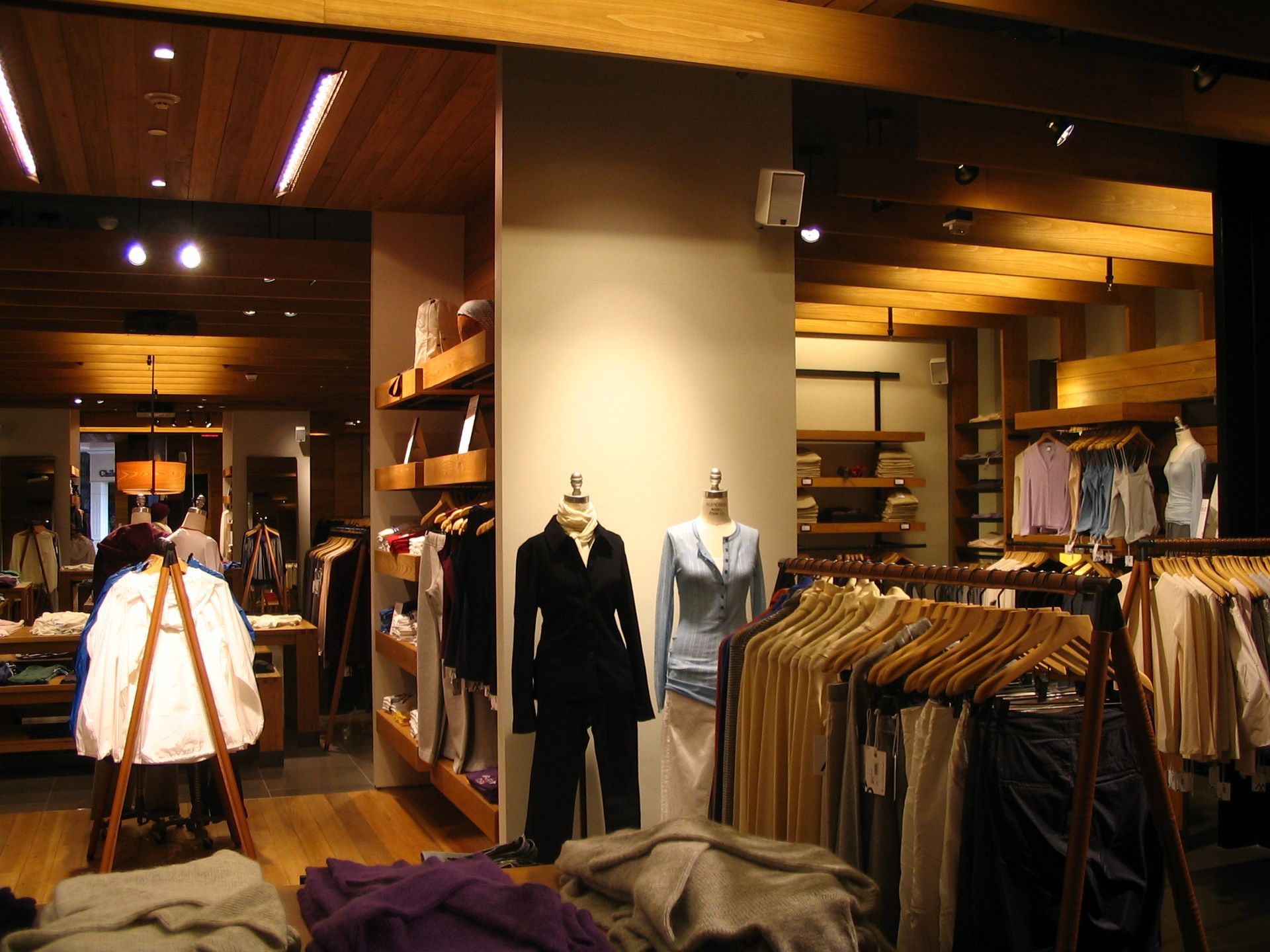 Clothing store interior with clothing racks, mannequins wearing jackets, and wooden ceiling beams.