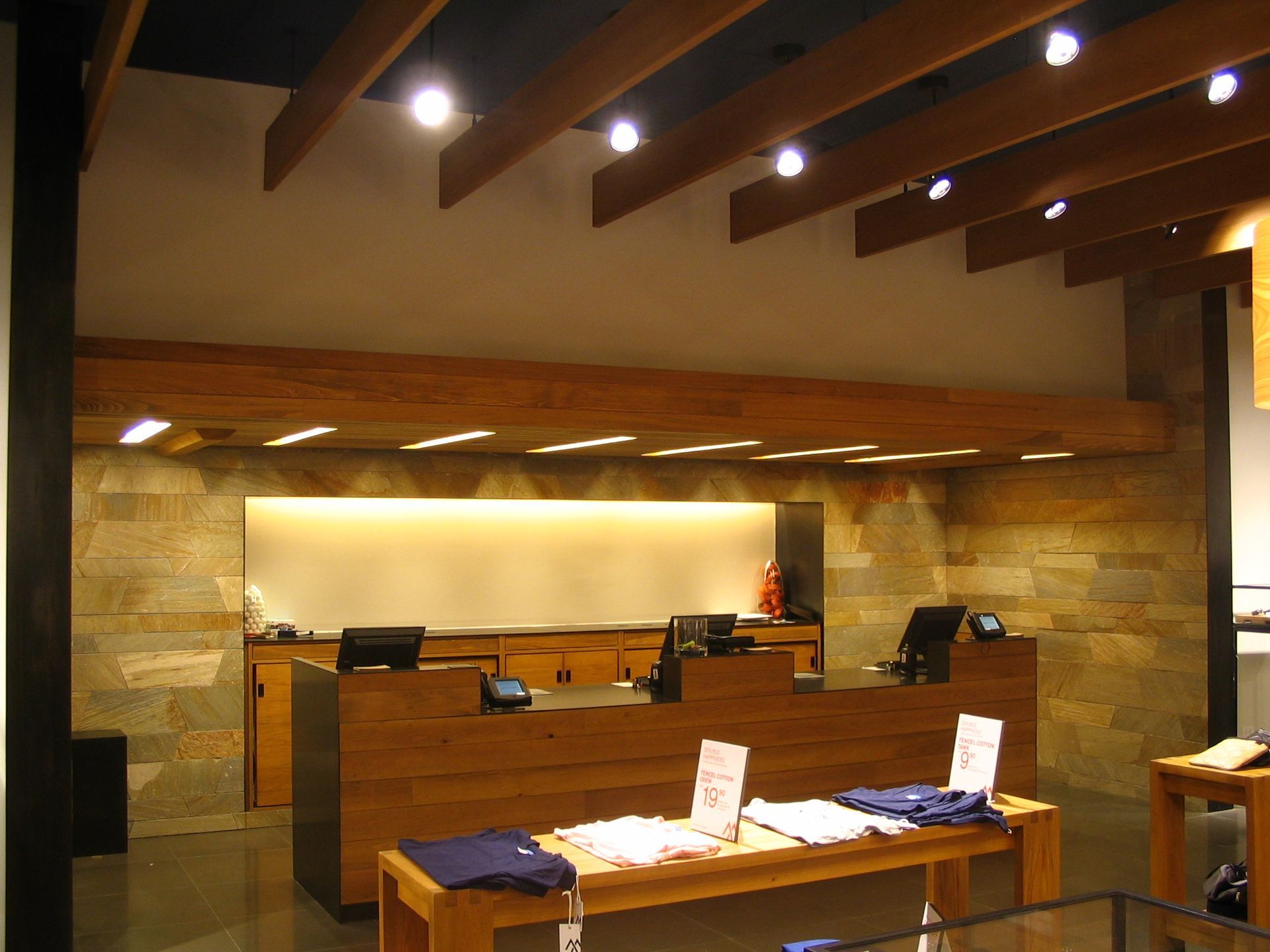 Cashier counter in a clothing store with wood and stone accents, illuminated by recessed lighting.