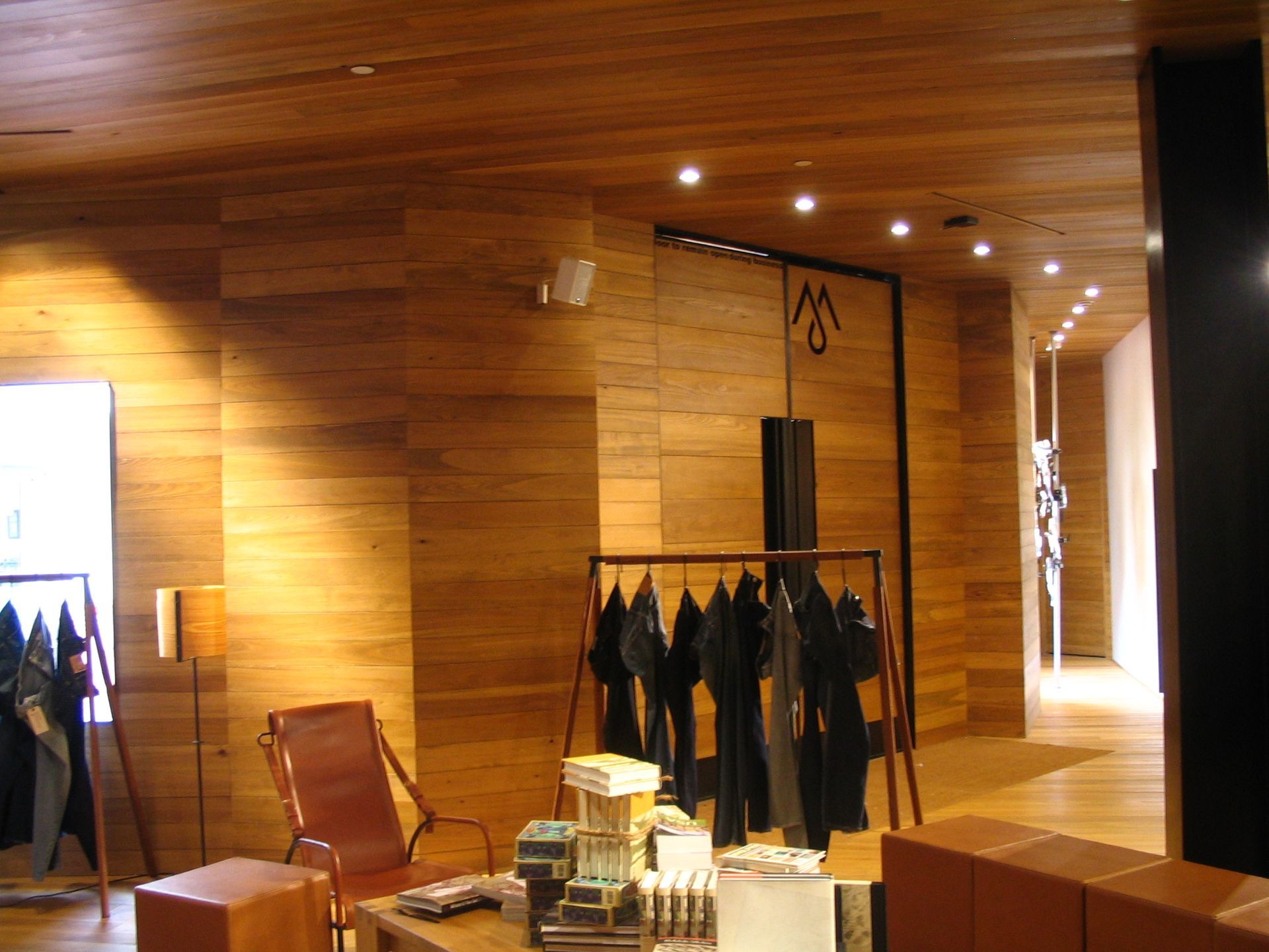 Wooden-walled clothing store interior with hanging garments, display table, and seating.