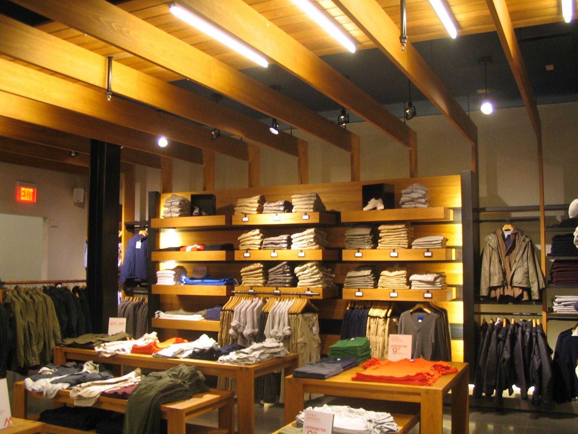 Clothing store interior with wooden shelving displaying folded shirts, clothing racks, and tables.