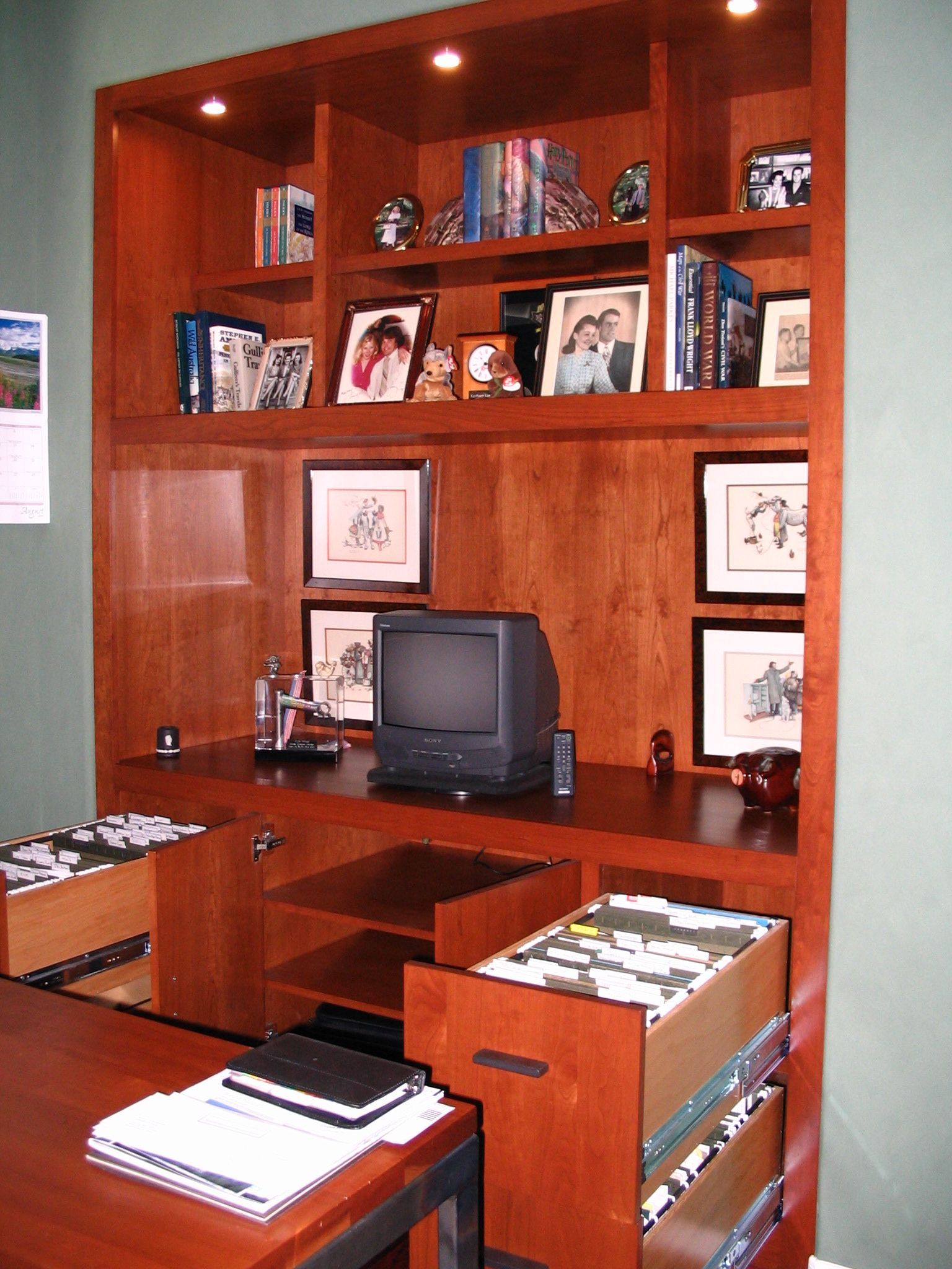 Built-in wooden home office with shelves, computer, and file drawers.