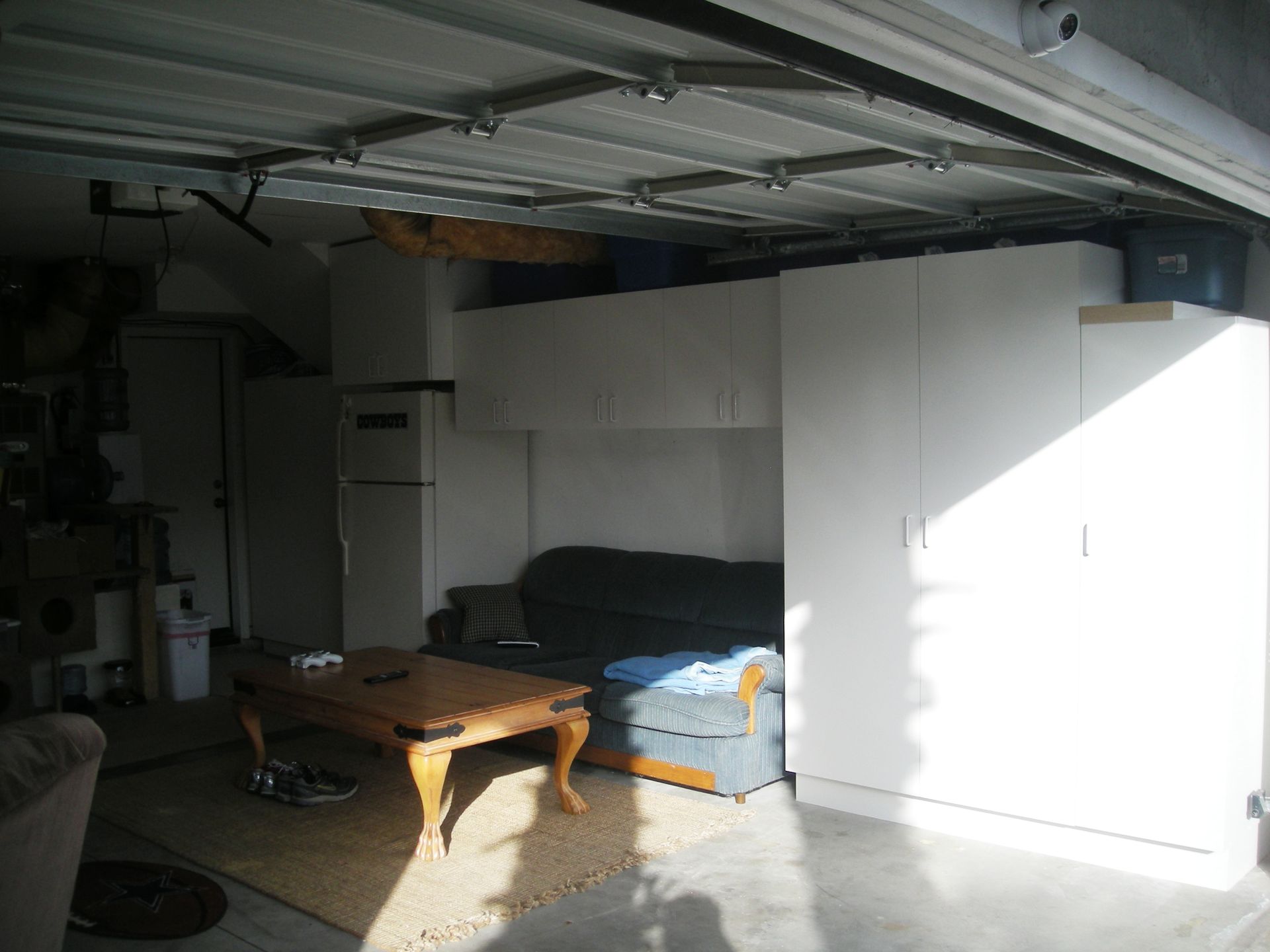 Garage interior with sofa, storage cabinets, and open garage door.