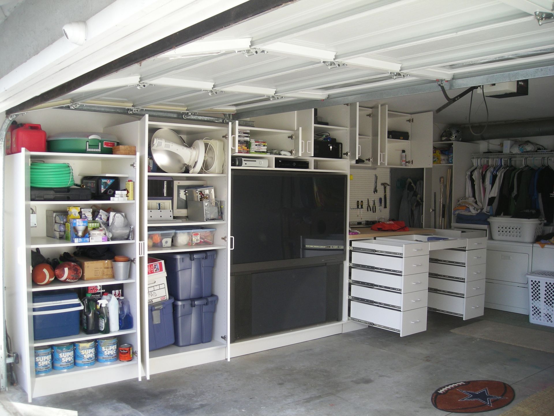 Garage interior with built-in white cabinets, shelves, and drawers, organizing various items against a white wall.