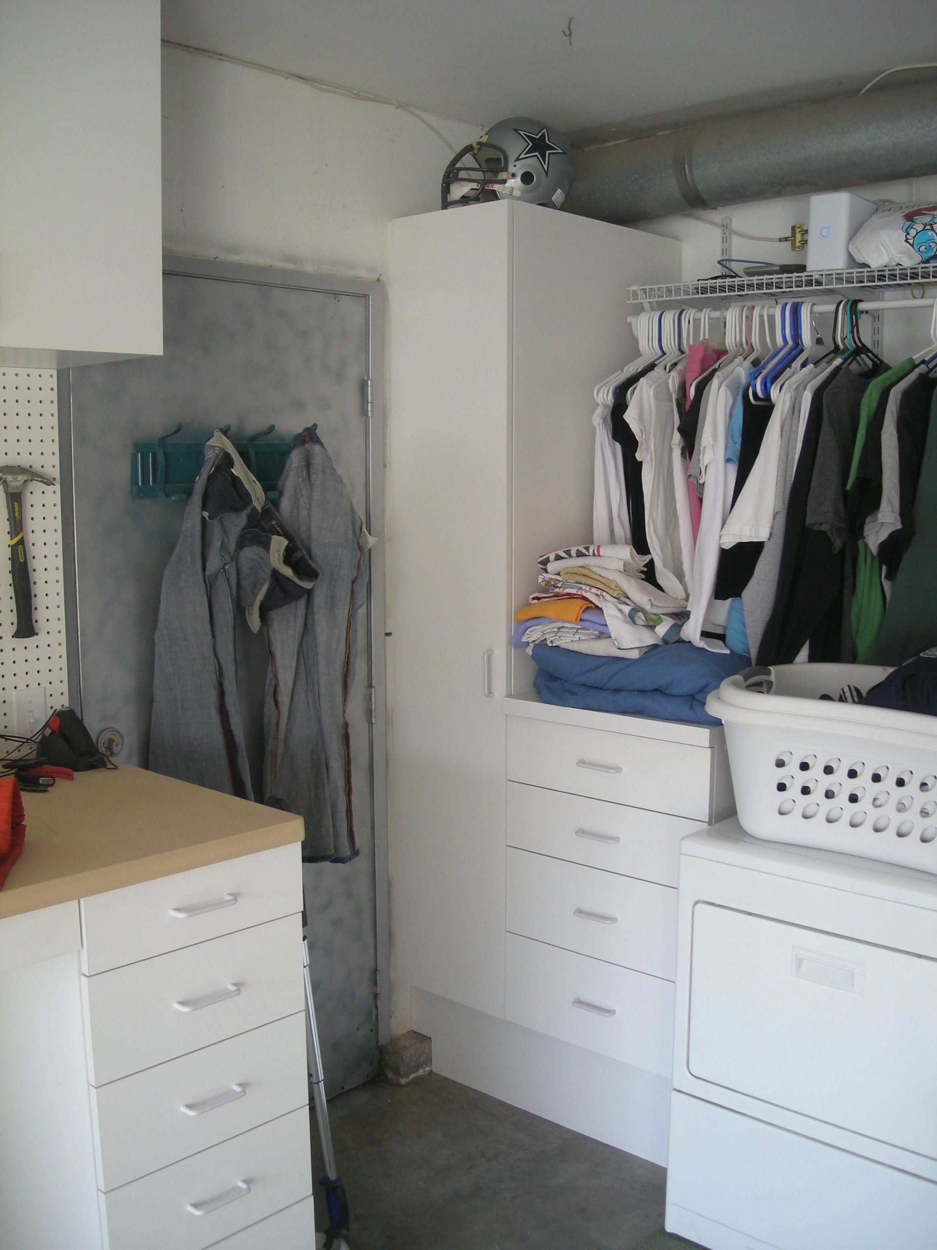 Garage interior with white cabinets, clothing rack, and laundry appliances. A helmet sits on top of a tall cabinet.