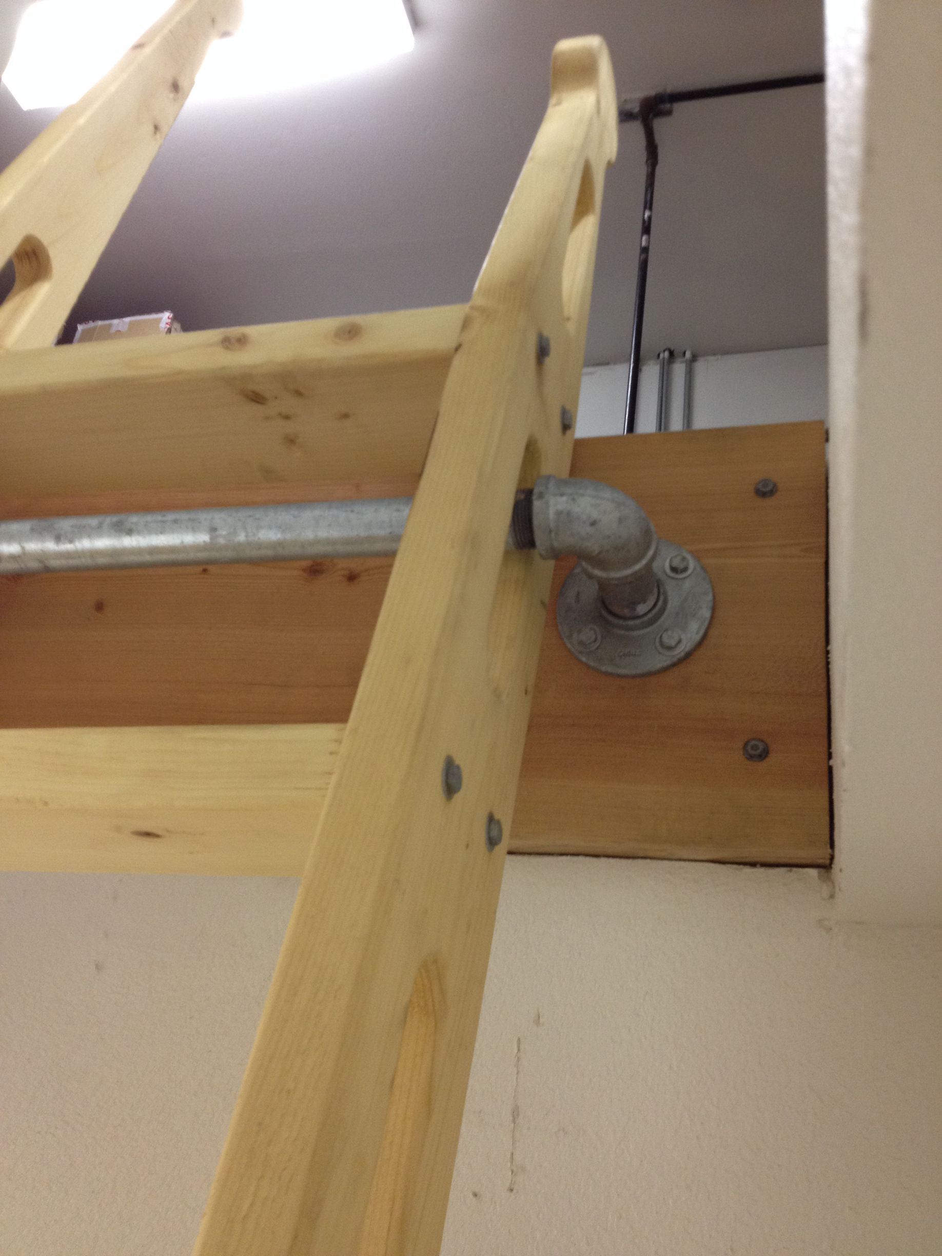Wooden ladder attached to a wall with metal piping and elbow joint for added support.