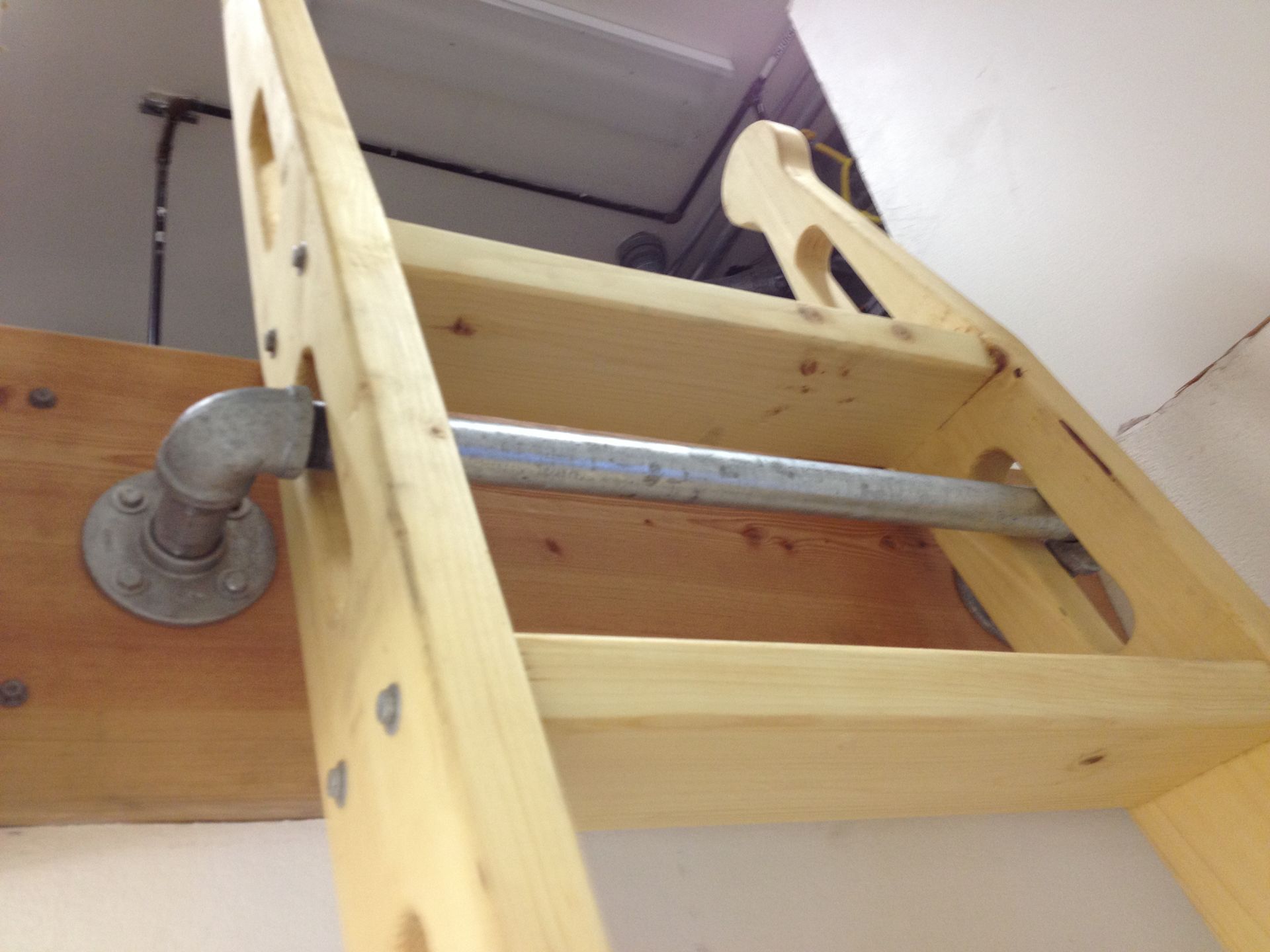 Wooden ladder leading to an opening in the ceiling, with metal pipe steps and hardware.
