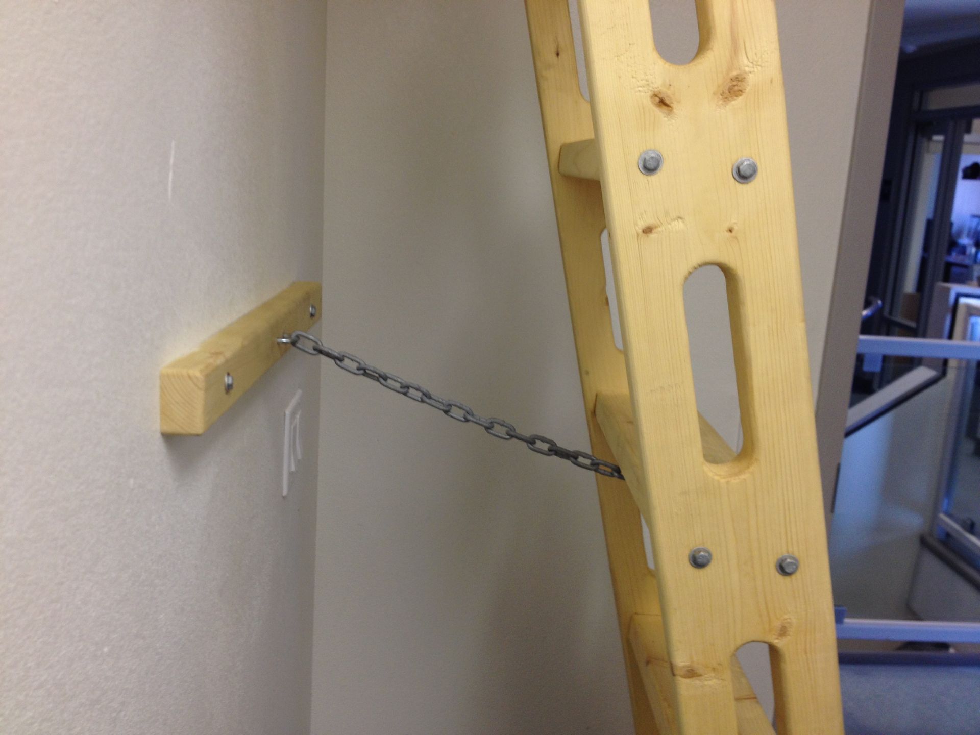 A wooden ladder braced with a chain and wooden block against a wall.