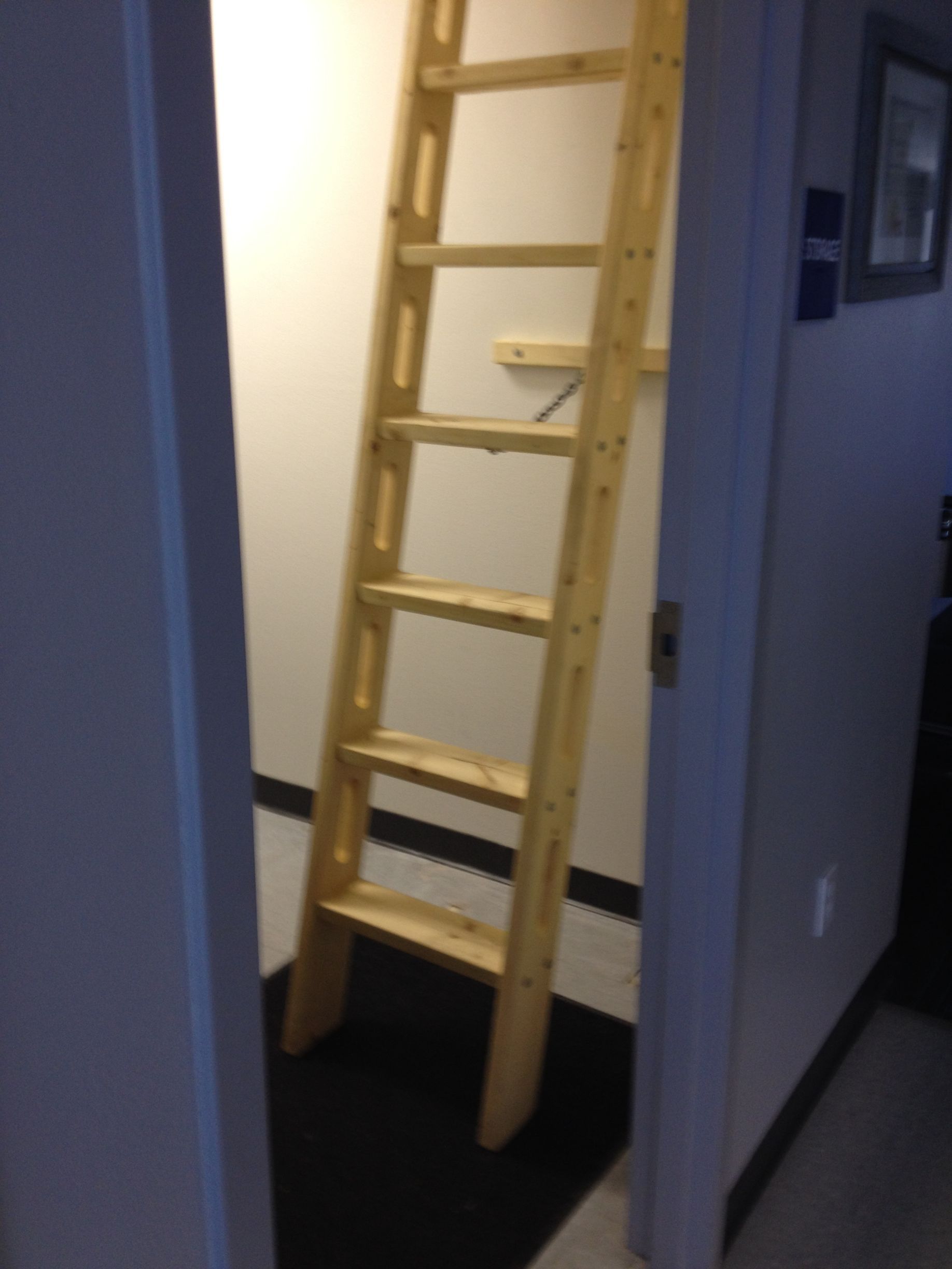 Wooden ladder leading up into a small, white-walled room.