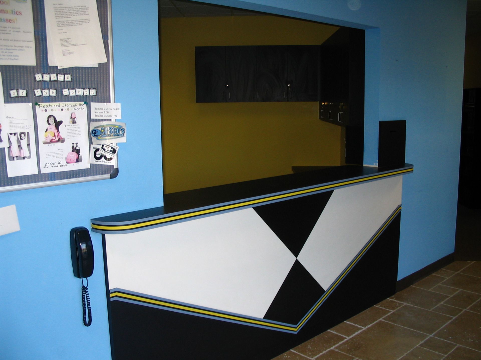 Reception desk with geometric black, white, and yellow design, mounted on blue wall, bulletin board to the left.