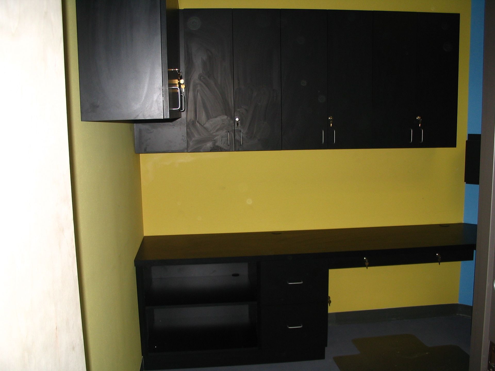 Black cabinets and desk against yellow wall. A blue doorway is in the background.