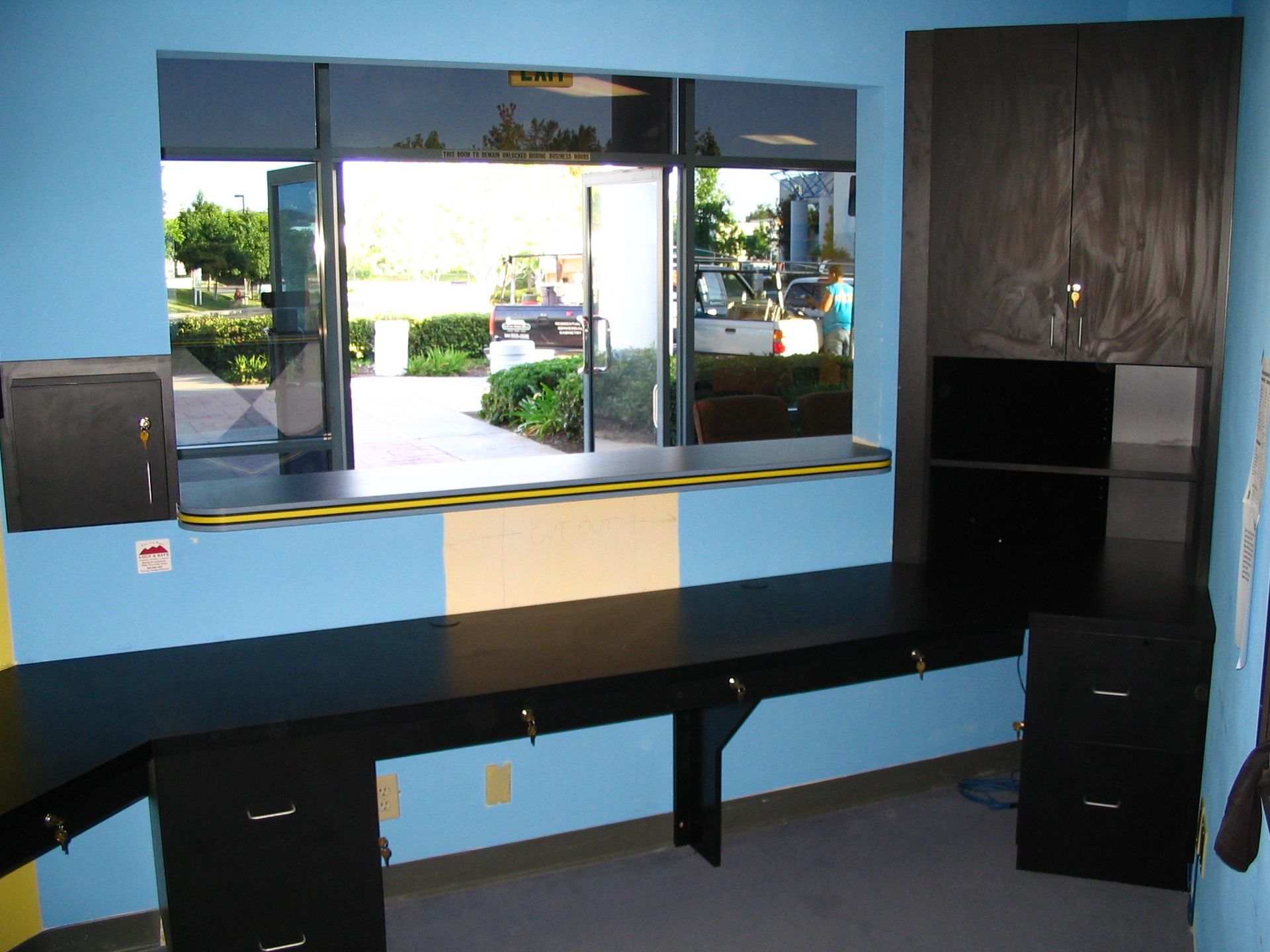 Office space with long black desk, blue walls, and large window overlooking outdoors.