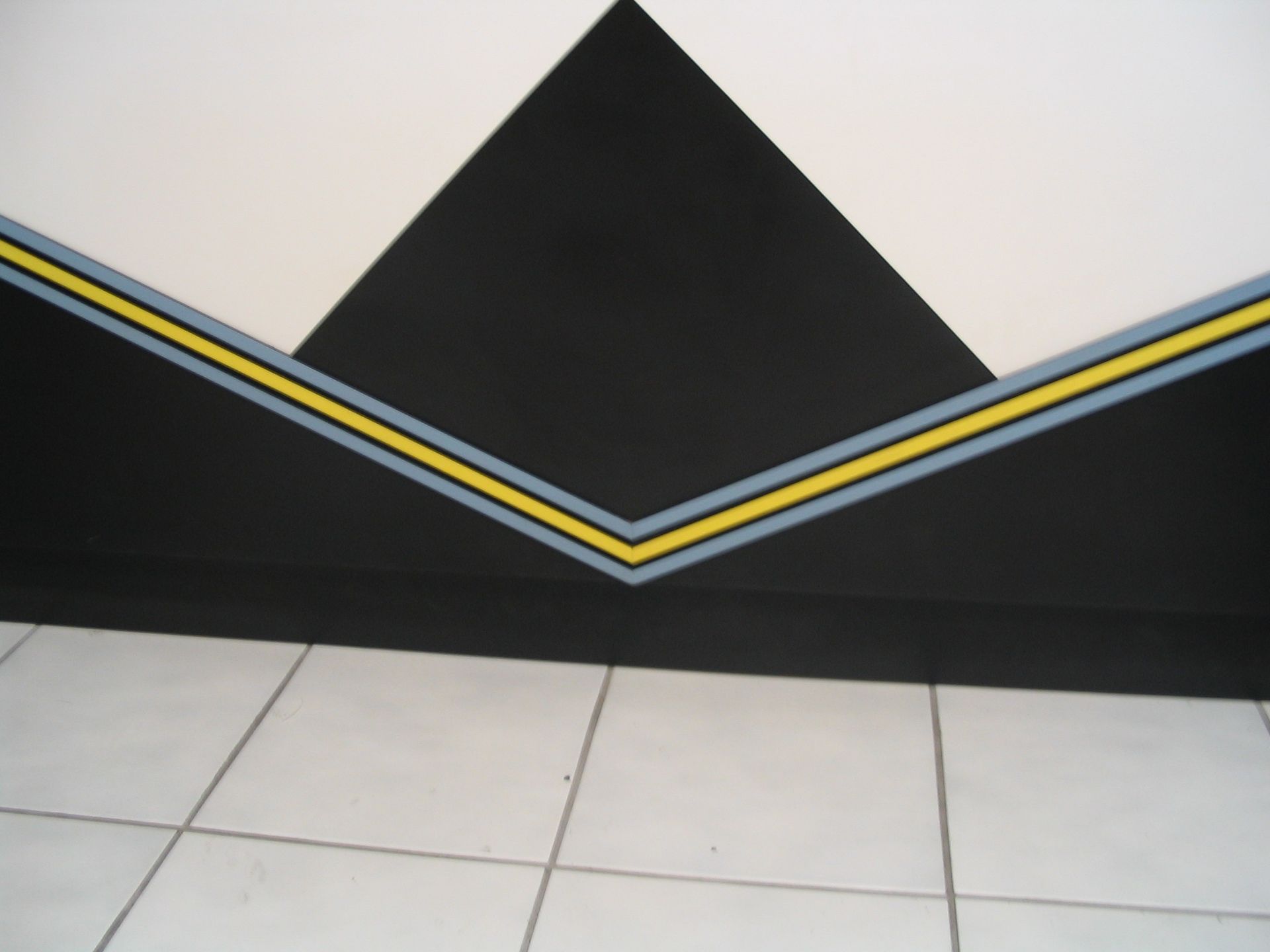 Black and white geometric wall design with a yellow and gray stripe detail, above white tiled floor.