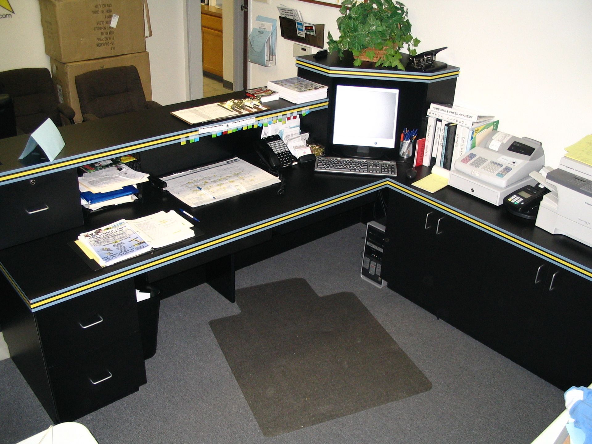 Black office desk with computer, printer, and cabinets, a plant, and papers.