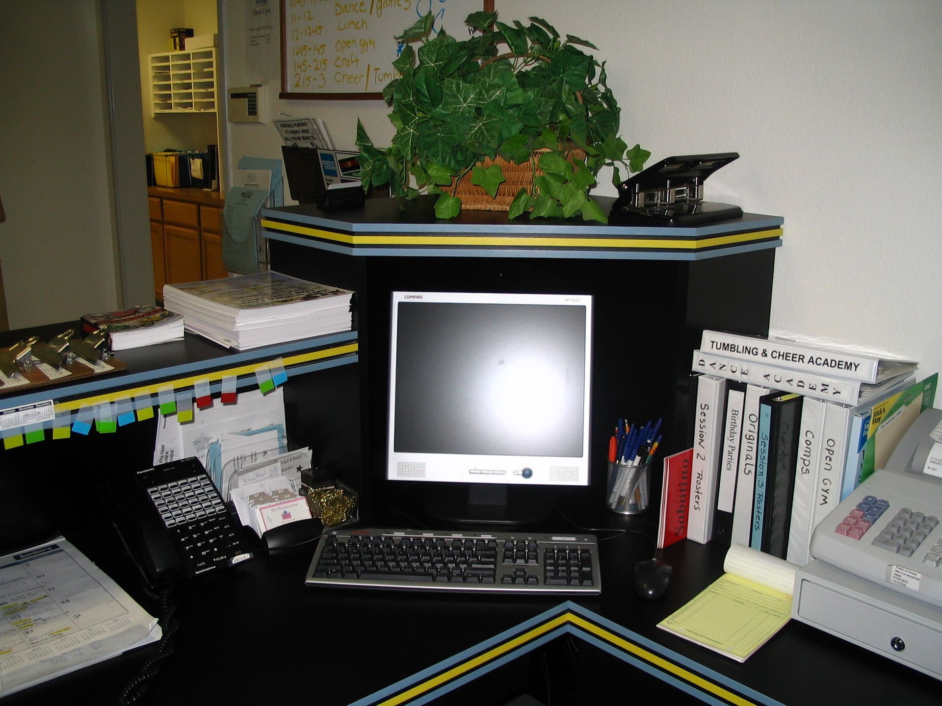 Office desk with computer, keyboard, books, and phone. Black desk with yellow and blue trim.