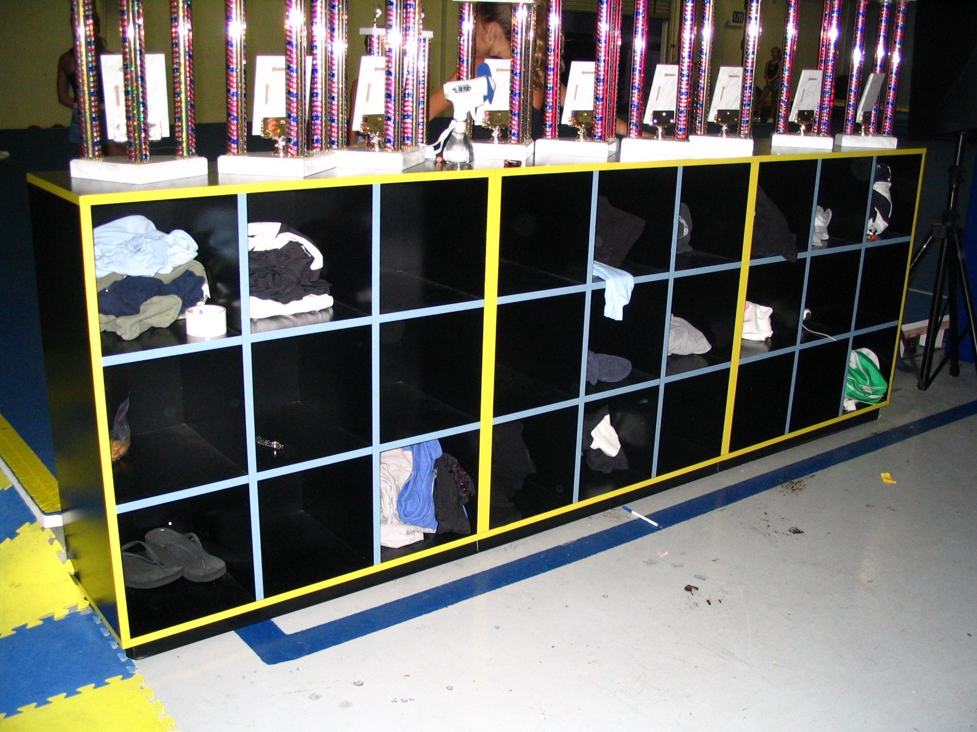 Black cubby shelves with yellow trim, filled with clothing. Trophies on top.