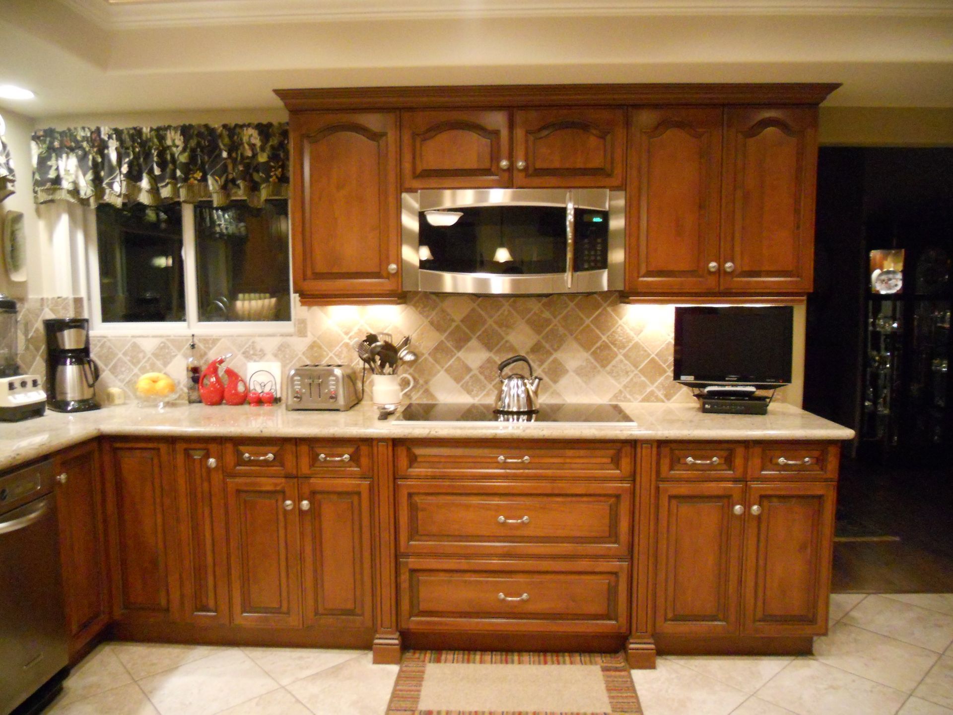 Kitchen with brown cabinets, backsplash, appliances, and off-white countertop, with window, and rug.