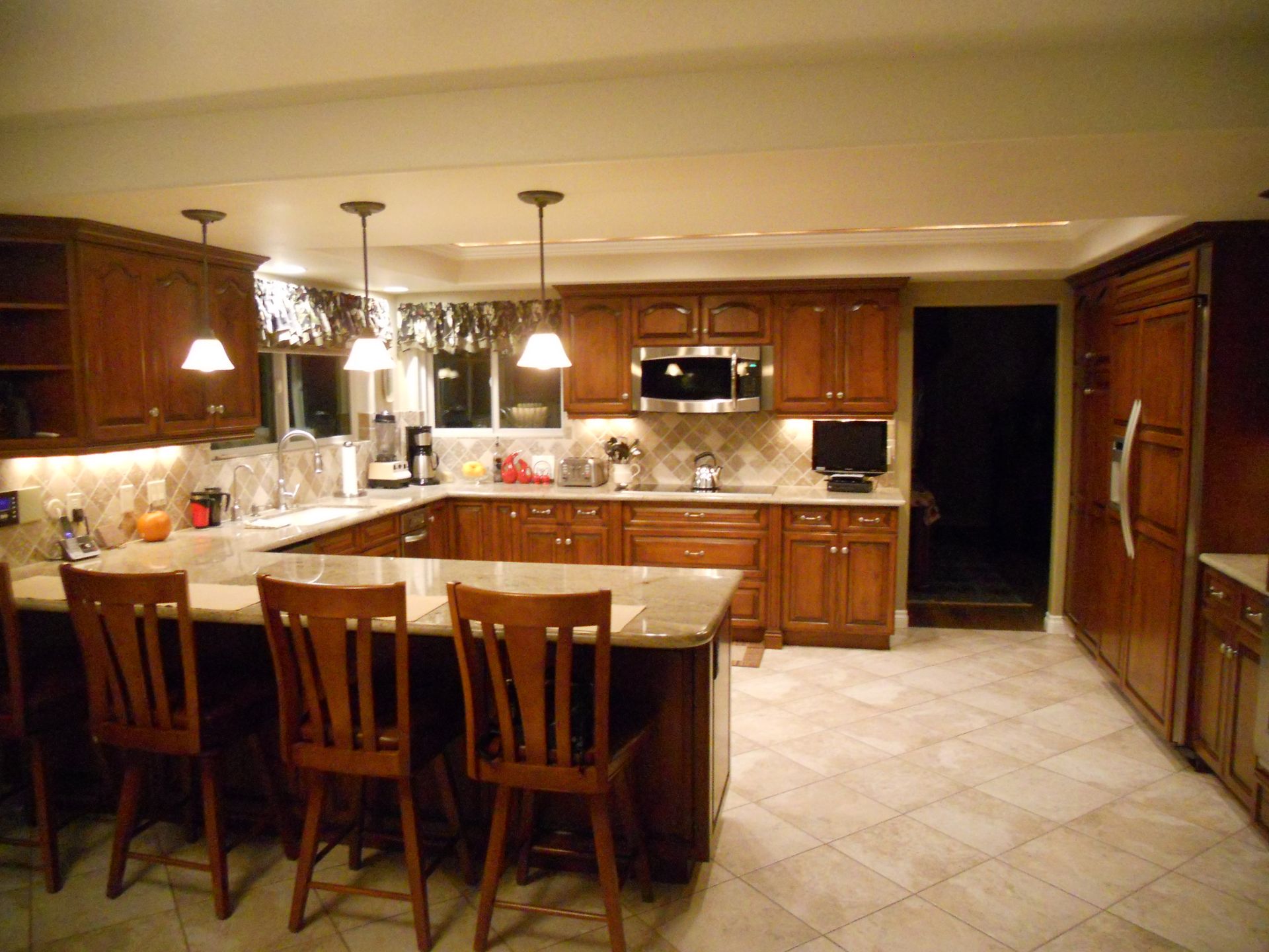 Kitchen with dark wood cabinets, granite countertops, and tile floor, lit by pendant lights.