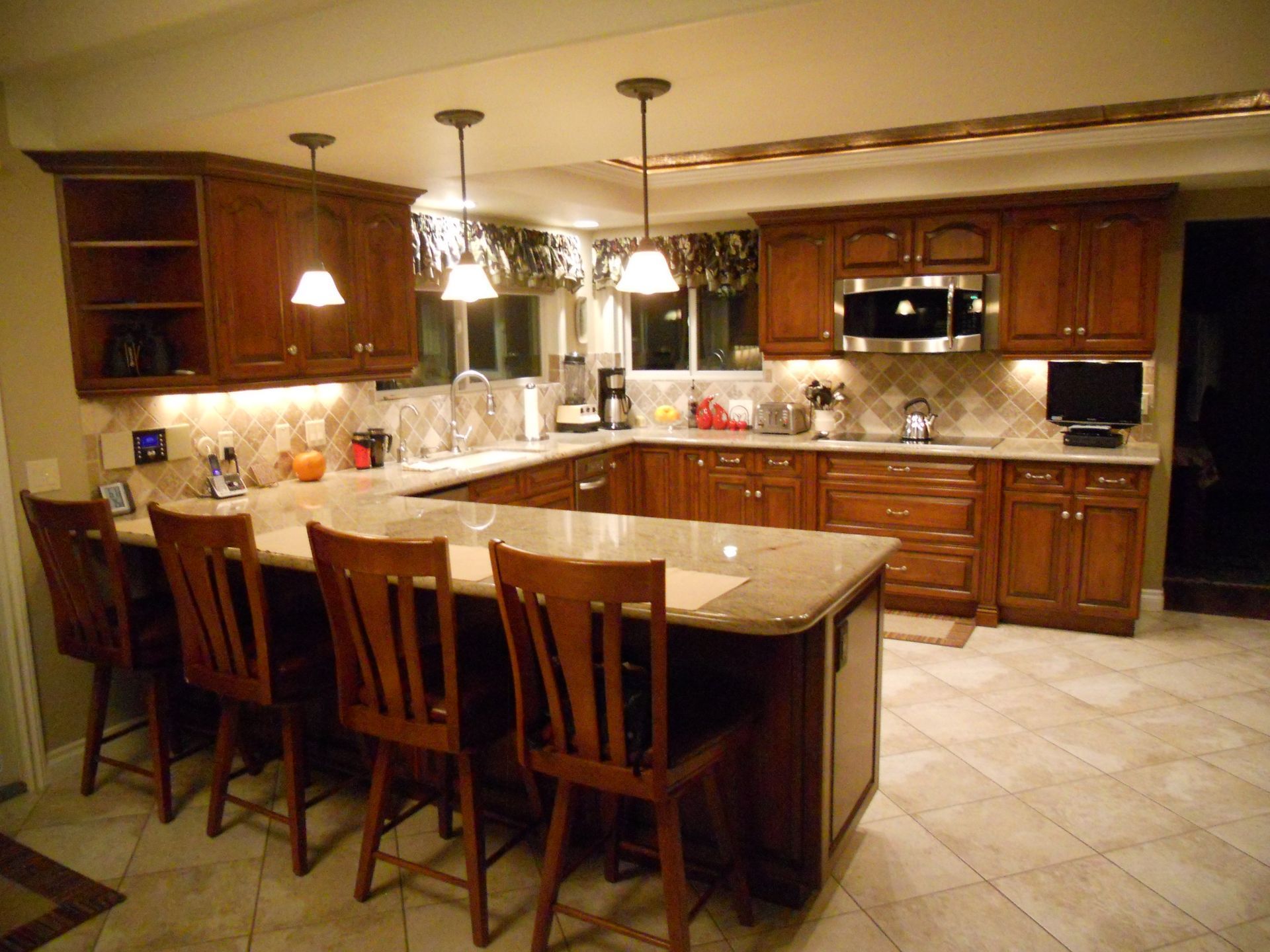 U-shaped kitchen with brown cabinets, granite countertops, and bar seating. Soft lighting illuminates the space.