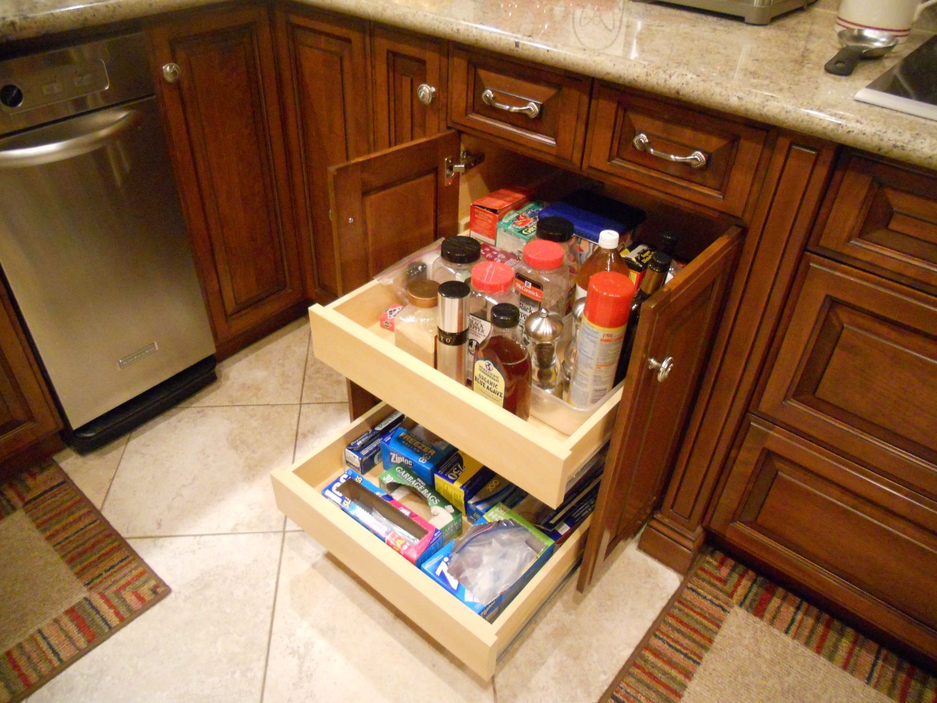 Open cabinet with pull-out spice rack and drawer in a kitchen. Wooden cabinets and a stainless steel dishwasher are visible.