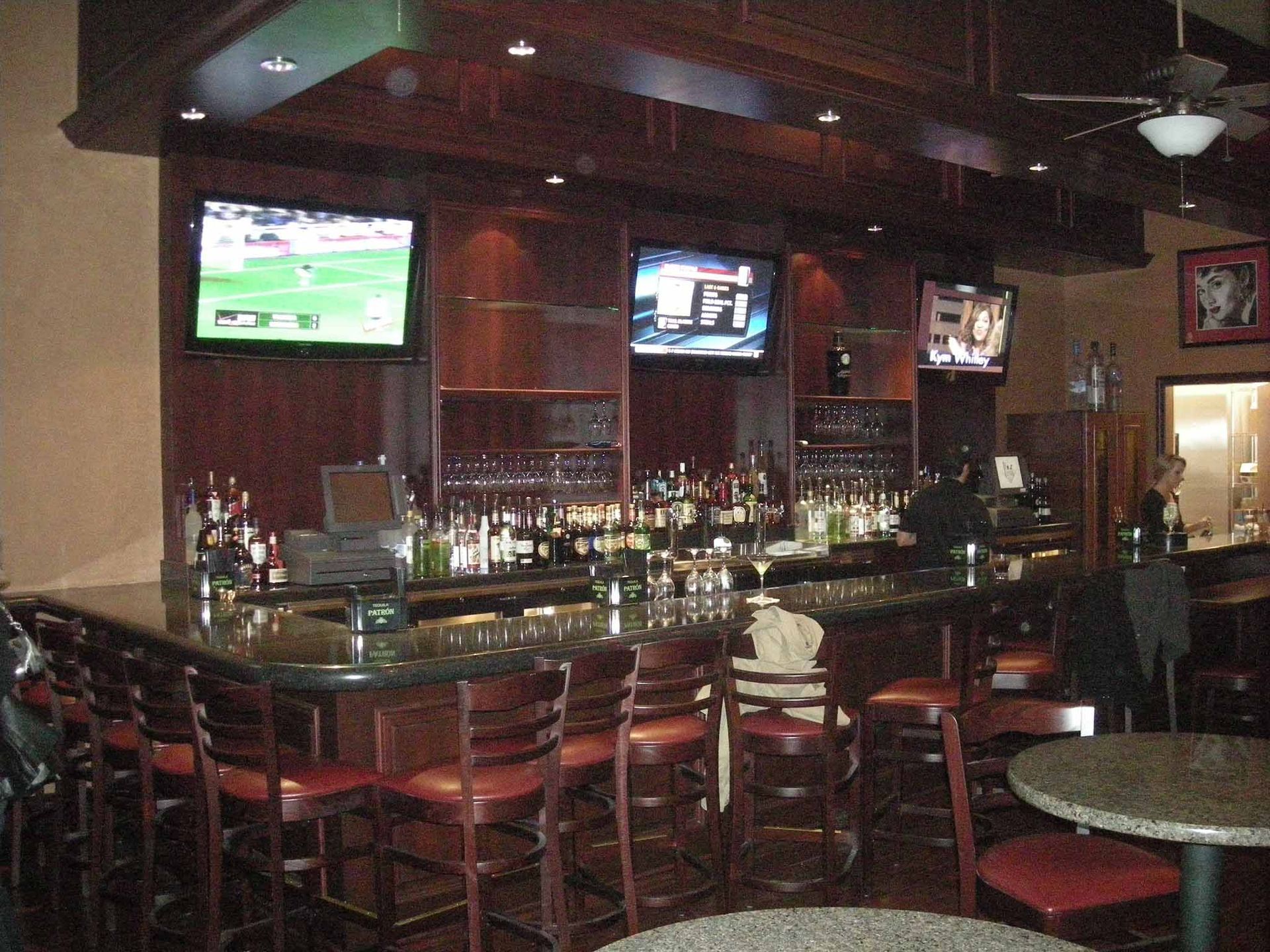 A bar with wooden interior, stools, TVs, and liquor bottles. Empty tables in the foreground.