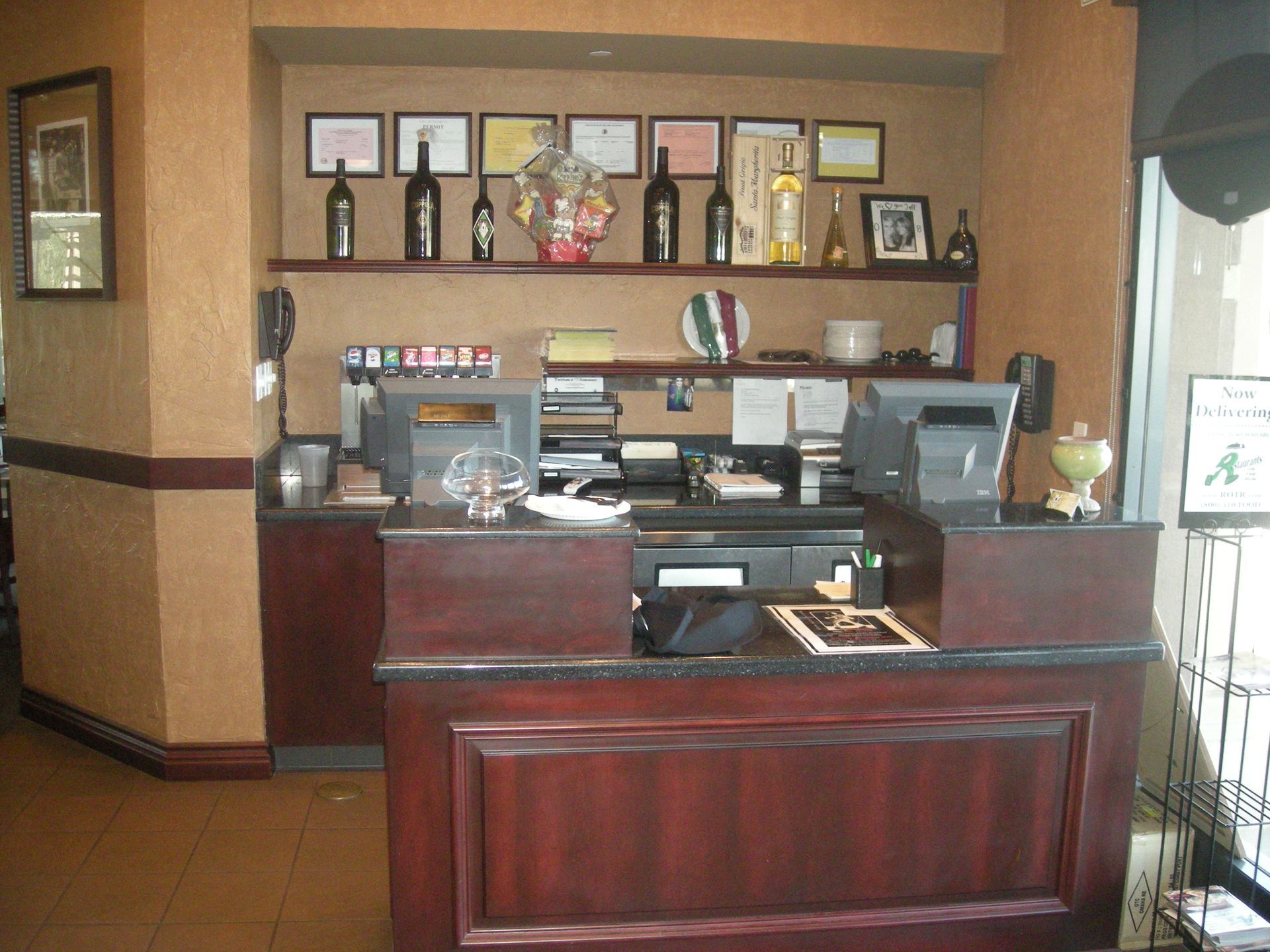 Restaurant host stand with computer, awards, and wine bottles on a shelf.