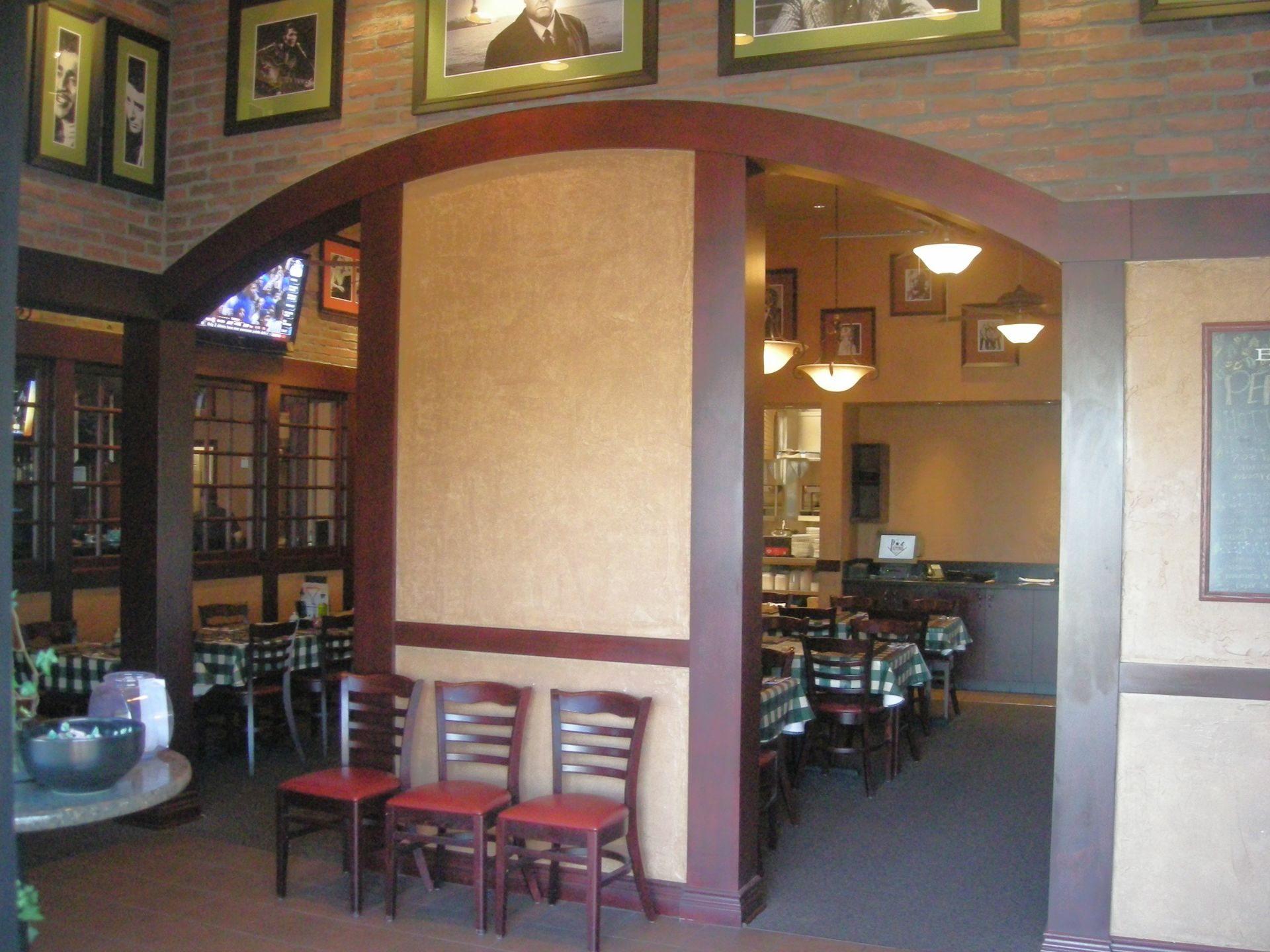 Restaurant interior with archway, tables, and chairs. Brick, wood, and tan walls with framed pictures.