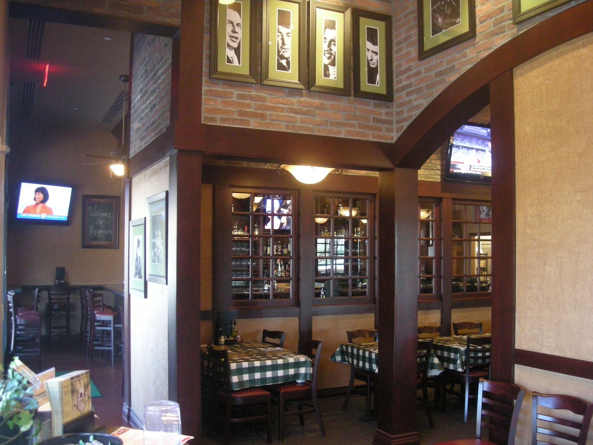 Interior of a restaurant with wooden beams, tables with checkered tablecloths, and framed pictures on brick walls.