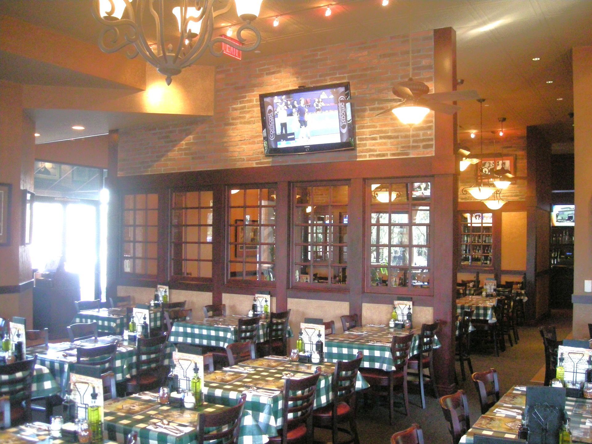 Restaurant interior with tables set for dining; green and white checkered tablecloths; dark wood accents; overhead lighting.