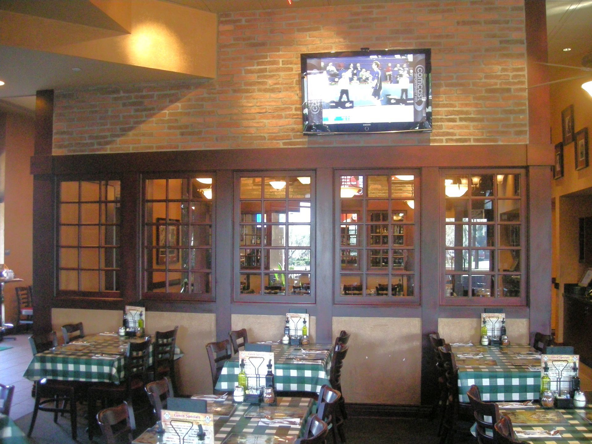 Restaurant dining area with tables, windows, and TV screen on a brick wall.