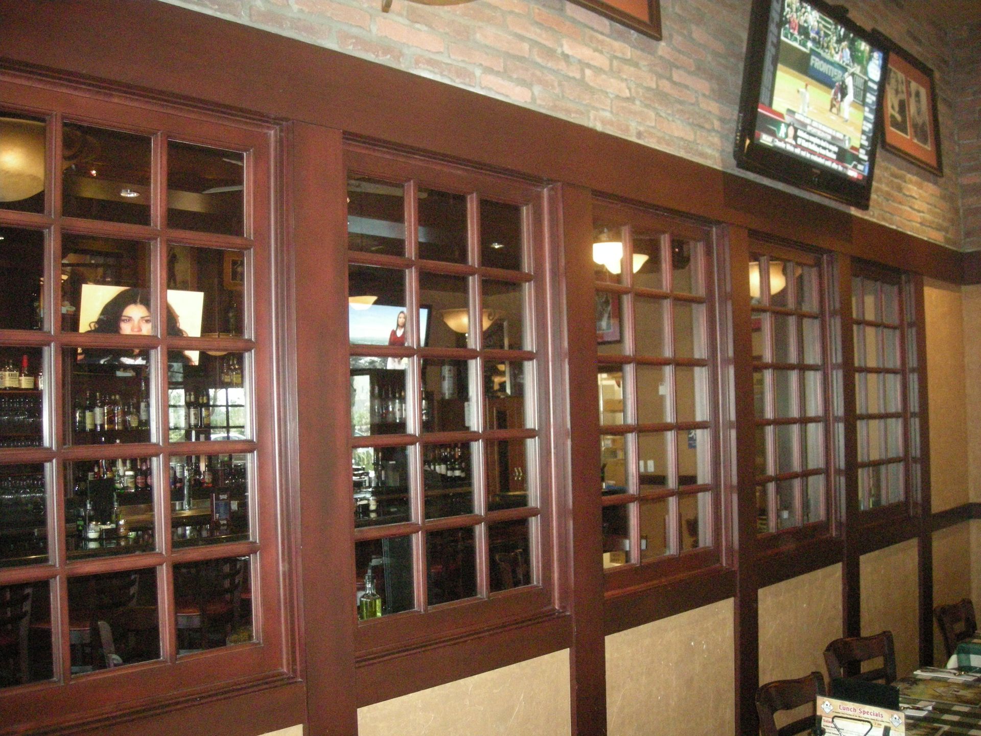 Interior restaurant view: Multiple dark-framed windows with grid patterns, reflecting the bar's interior; TV screen above.
