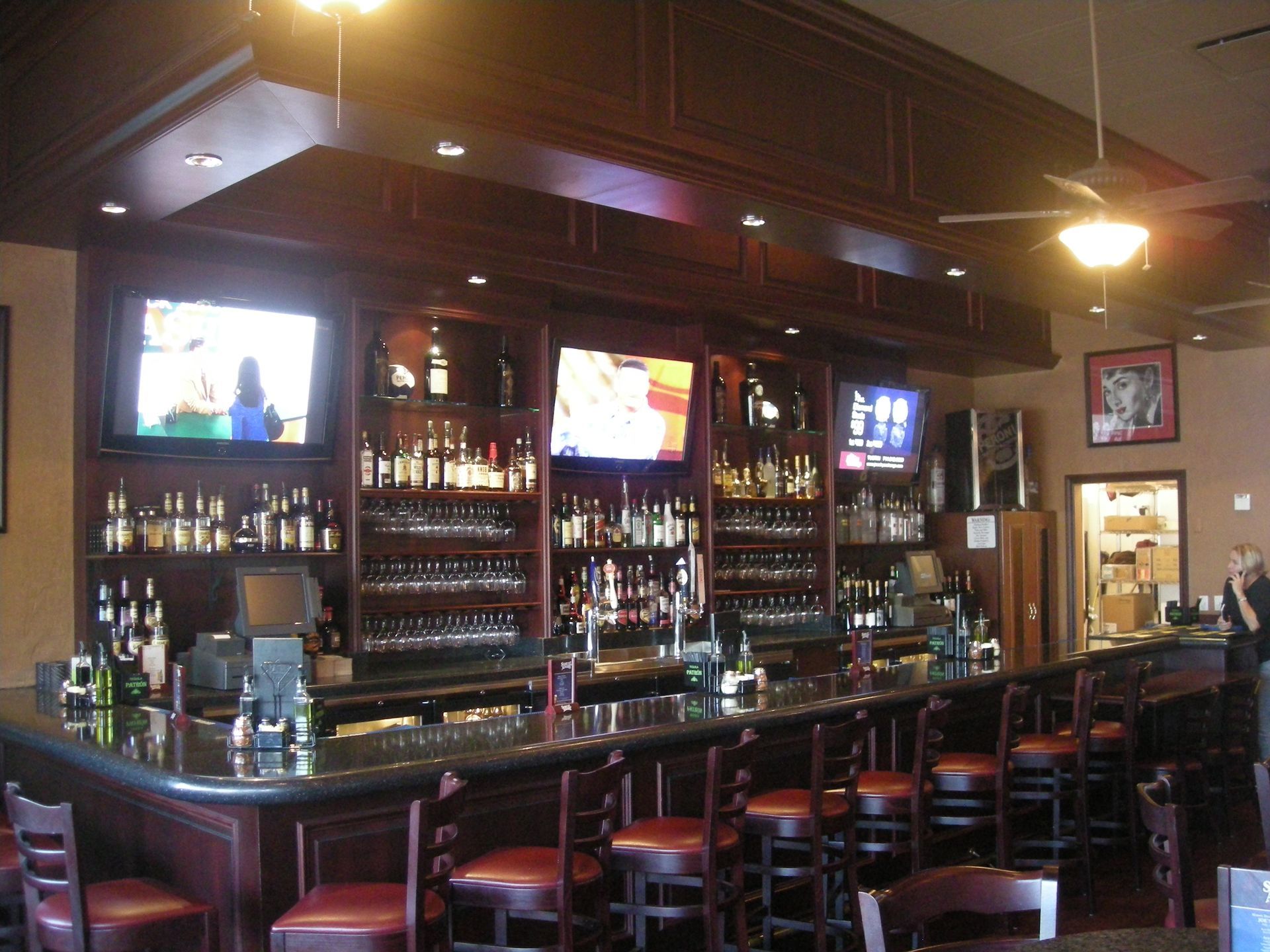 Interior bar with dark wood, liquor bottles, TVs, stools, and a person.