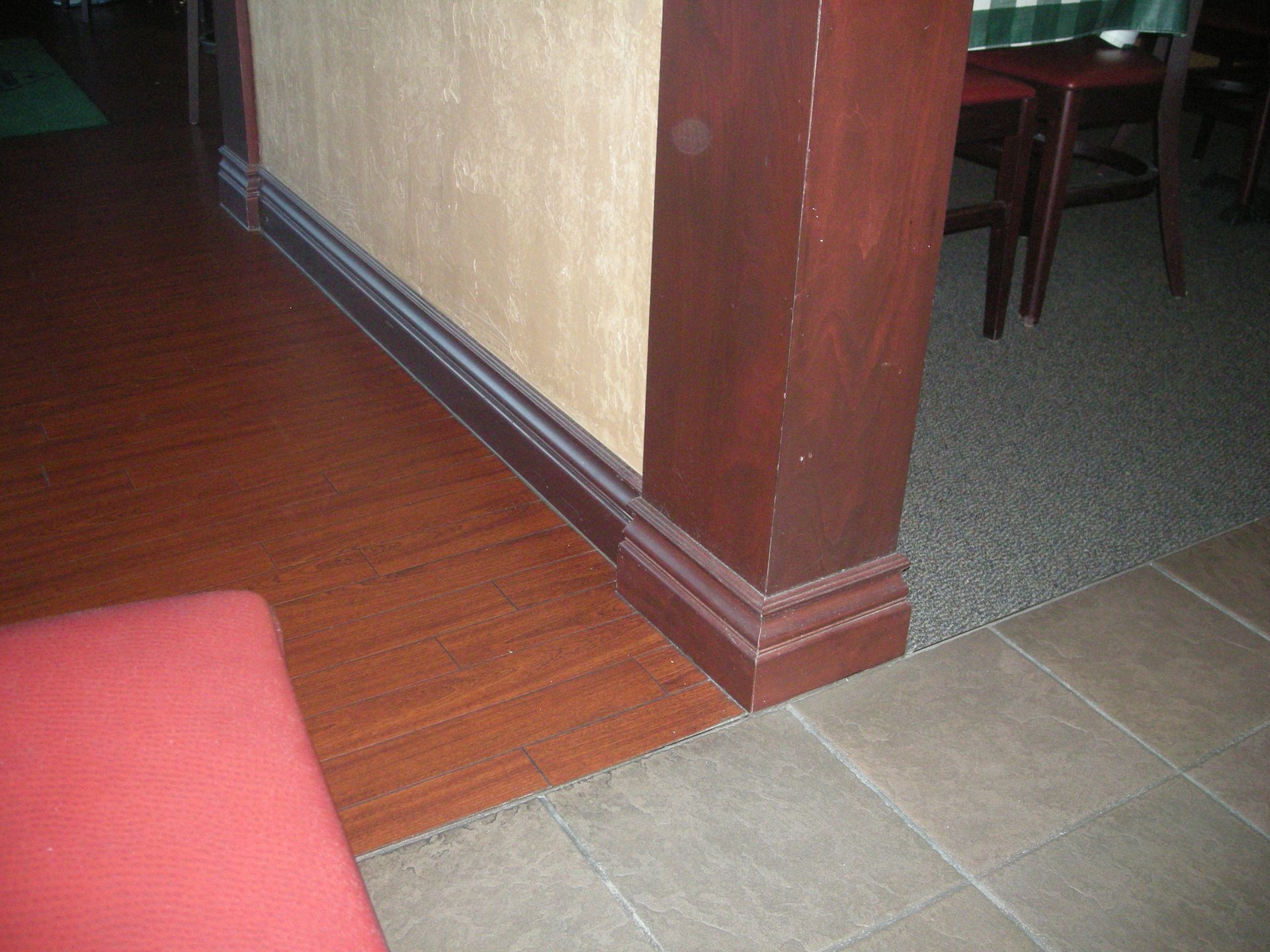 Wooden floor, wall, and pillar in a room with a brown/tan color scheme, featuring a red seat and tiled floor.