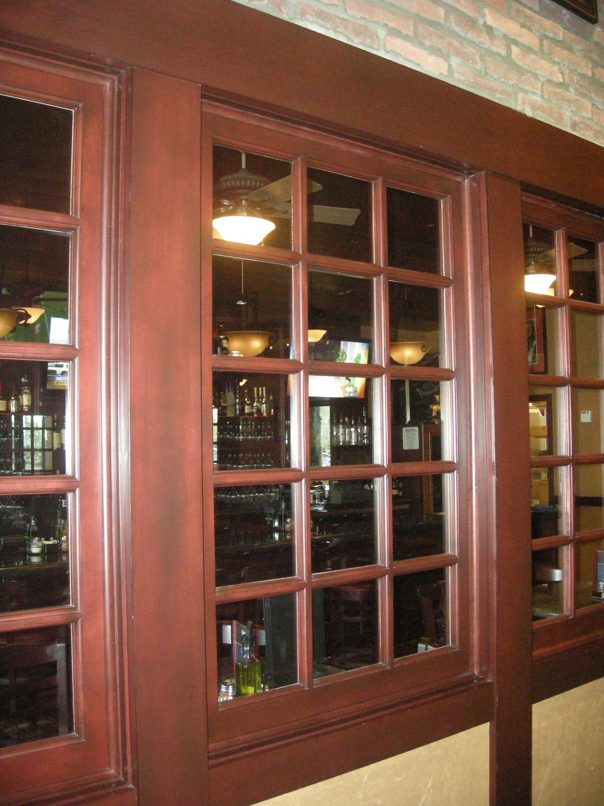 Brown-framed windows with multiple panes, reflecting a dimly lit interior with lights and bar.