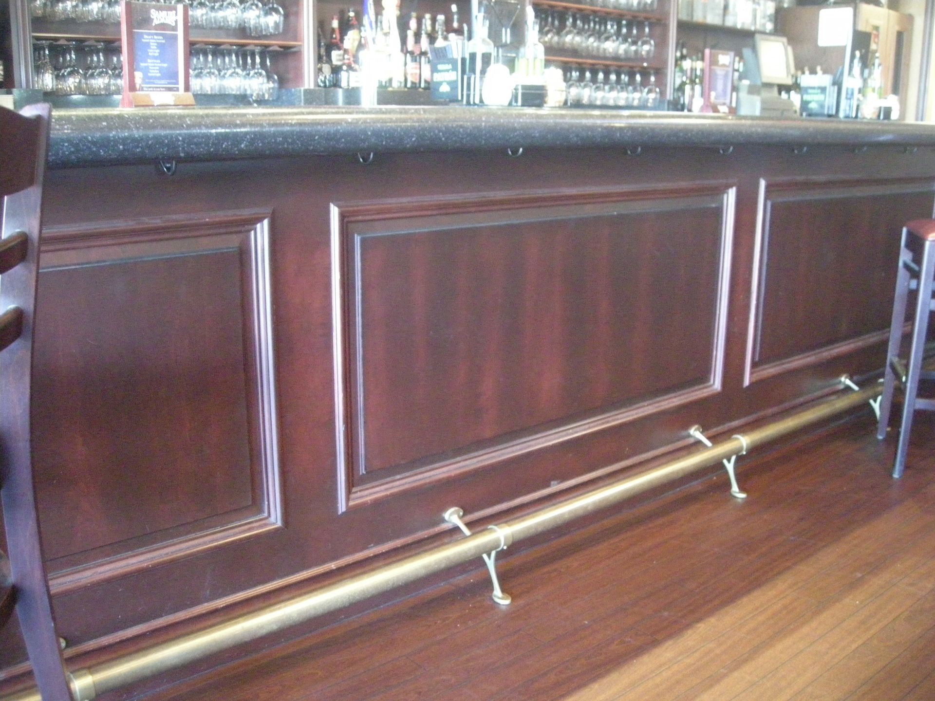 Wooden bar with brass foot rail, dark wood paneling, counter with bottles visible in background.