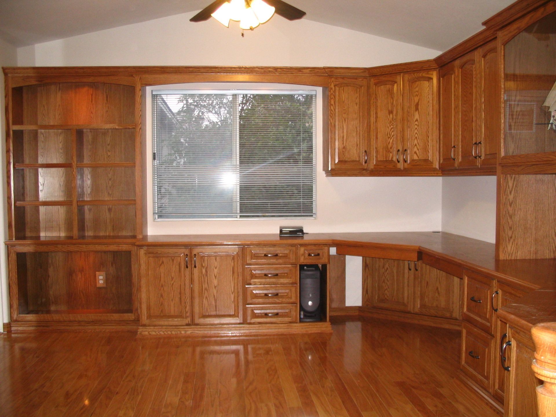 Built-in oak cabinetry and bookshelves surround a window in a room with hardwood floors.