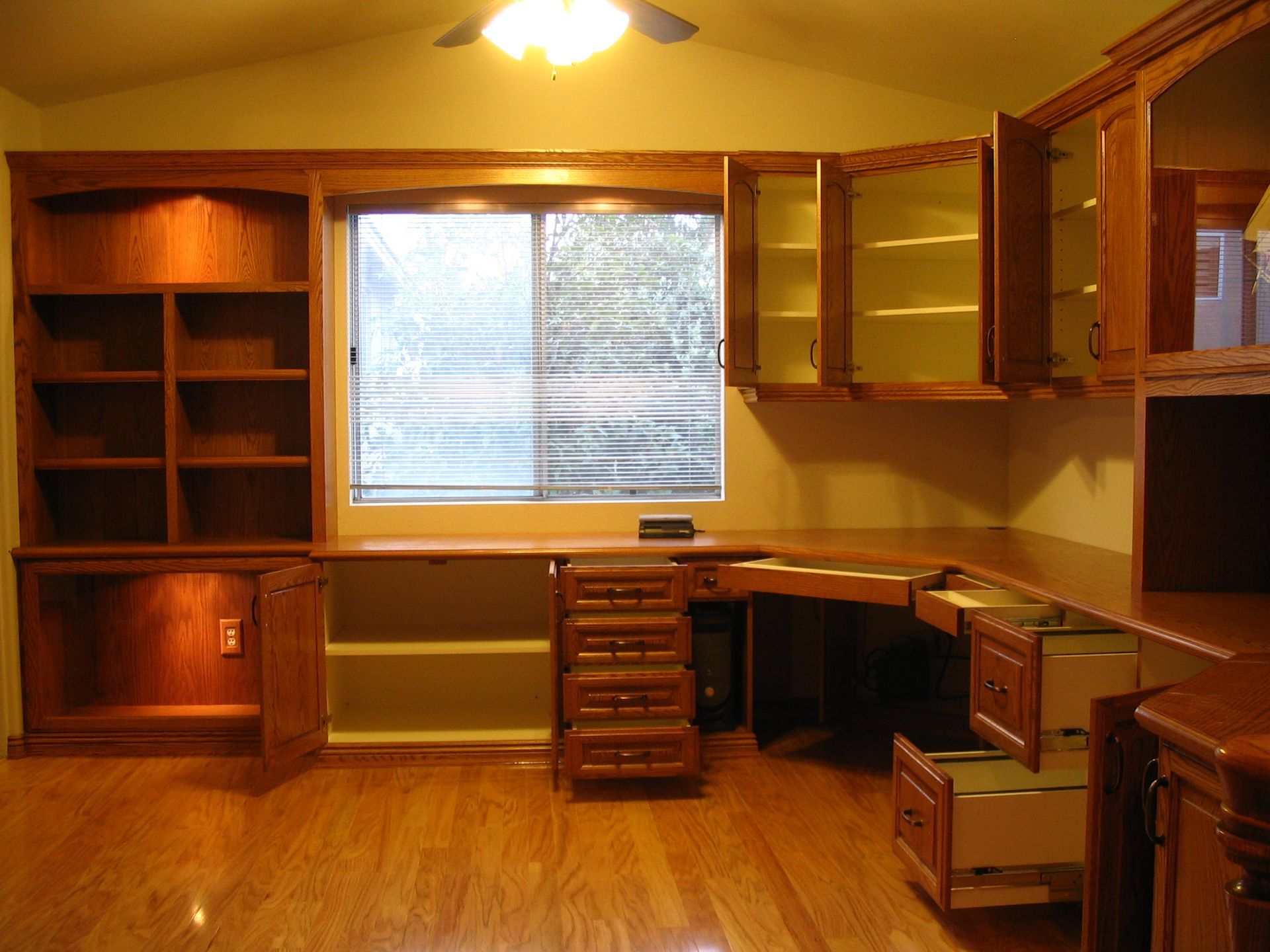 Wooden home office with built-in desk, shelves, and cabinets. Includes a window and a ceiling fan.