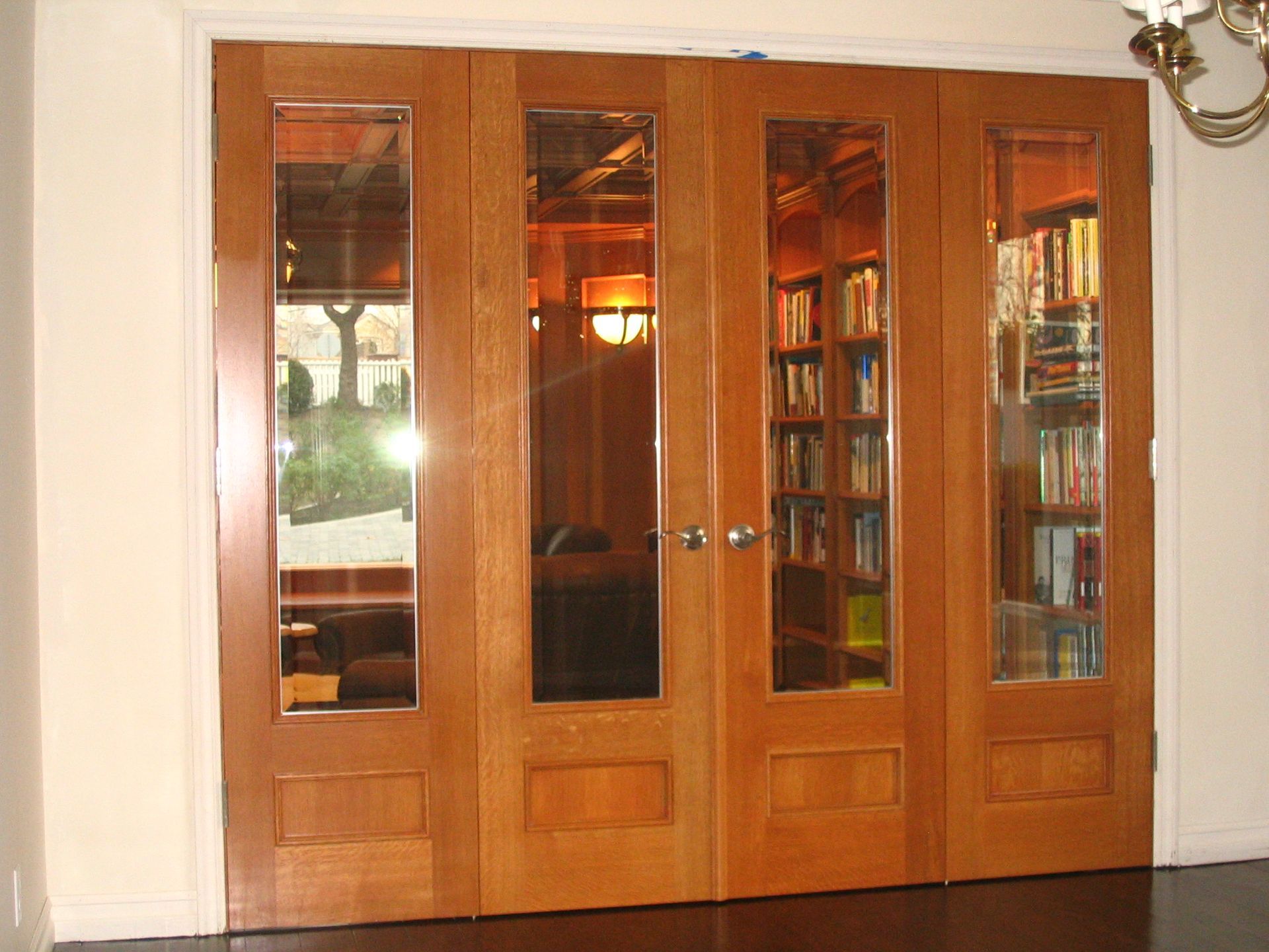 Four-panel wooden doors with glass panes, leading to a room with bookshelves and soft lighting.